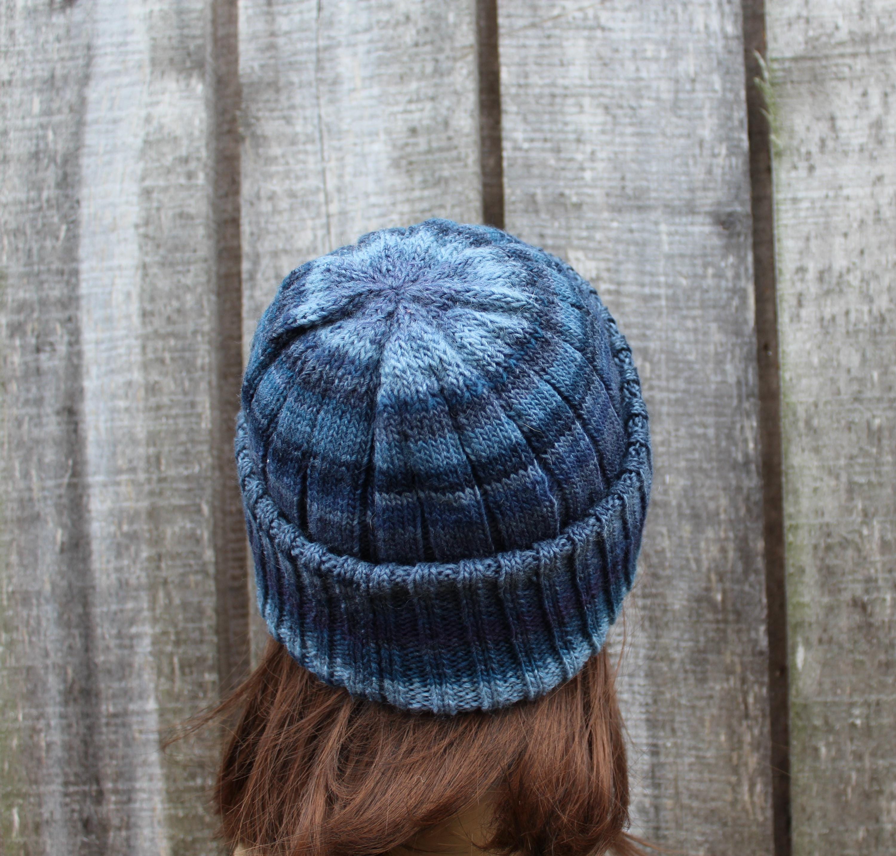 Blue knitted beanie worn by a person against a wooden fence background