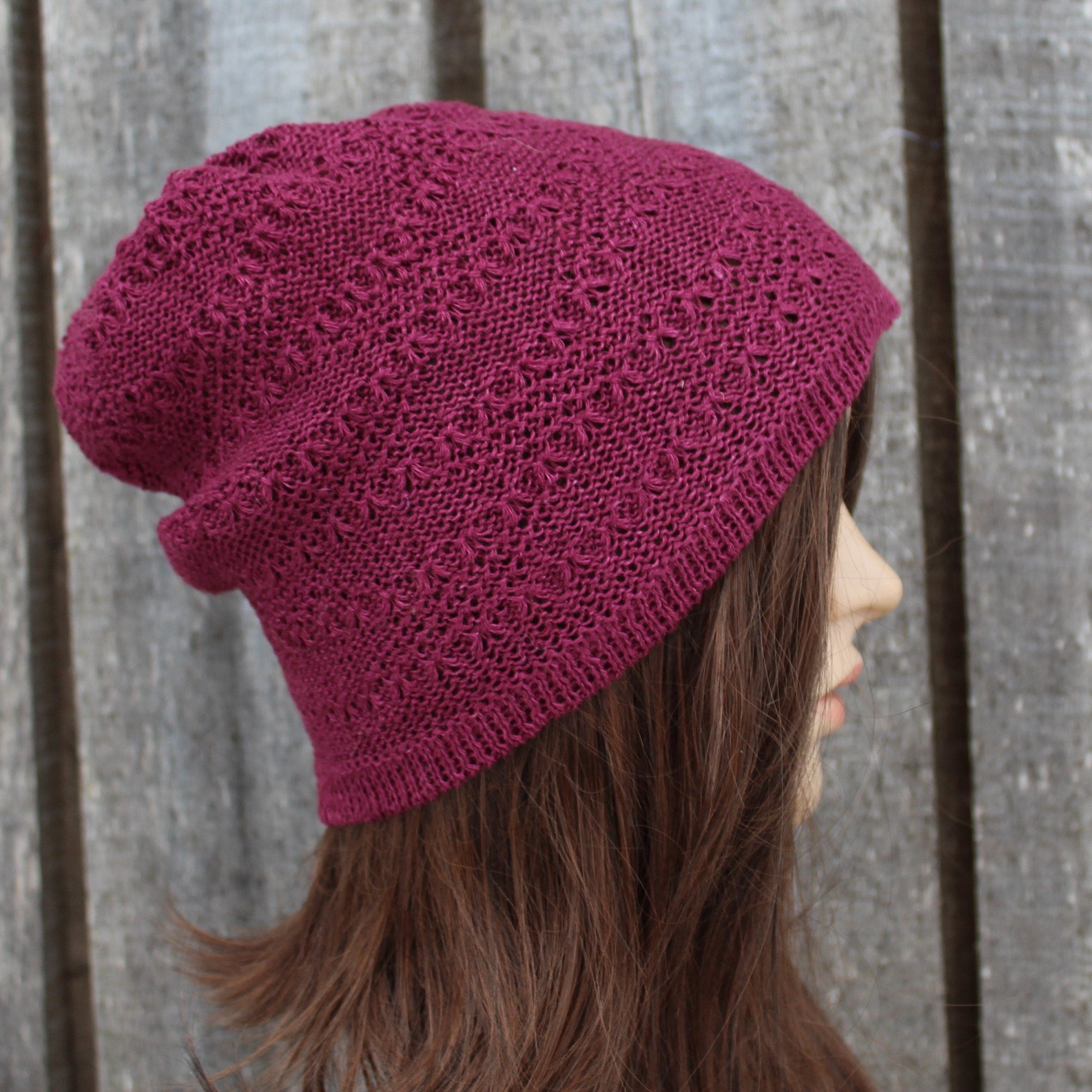 Person wearing a maroon knitted beanie against a wooden fence background