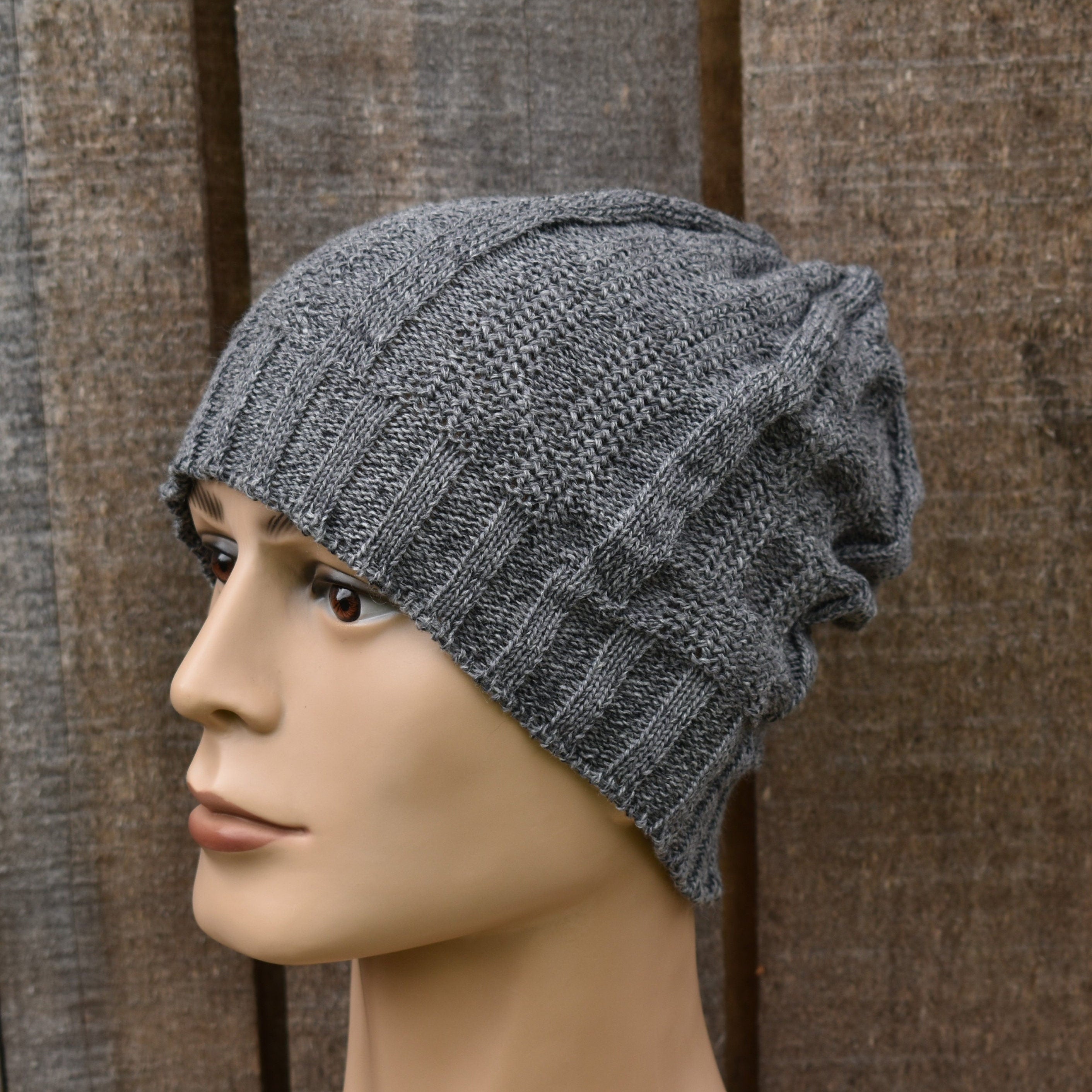 Mannequin head wearing a gray knit beanie against a wooden panel background