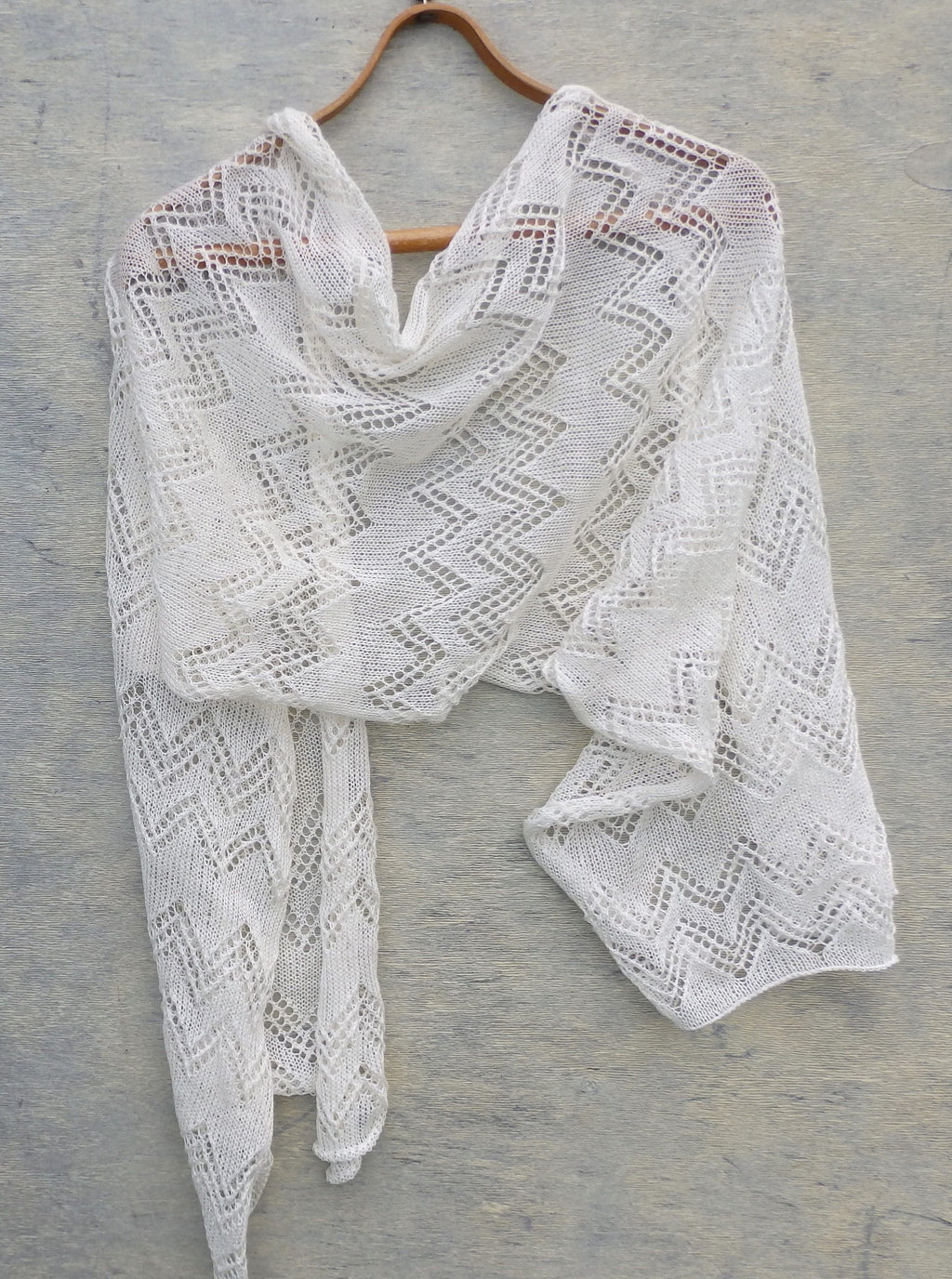 White knitted shawl on a wooden hanger against a gray background