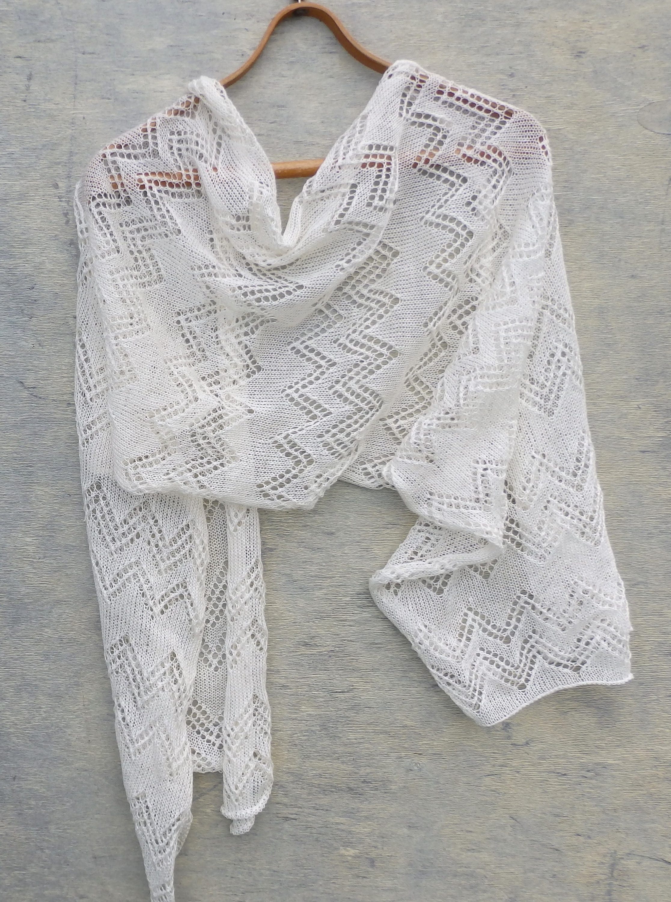 White knitted shawl on a wooden hanger against a gray background