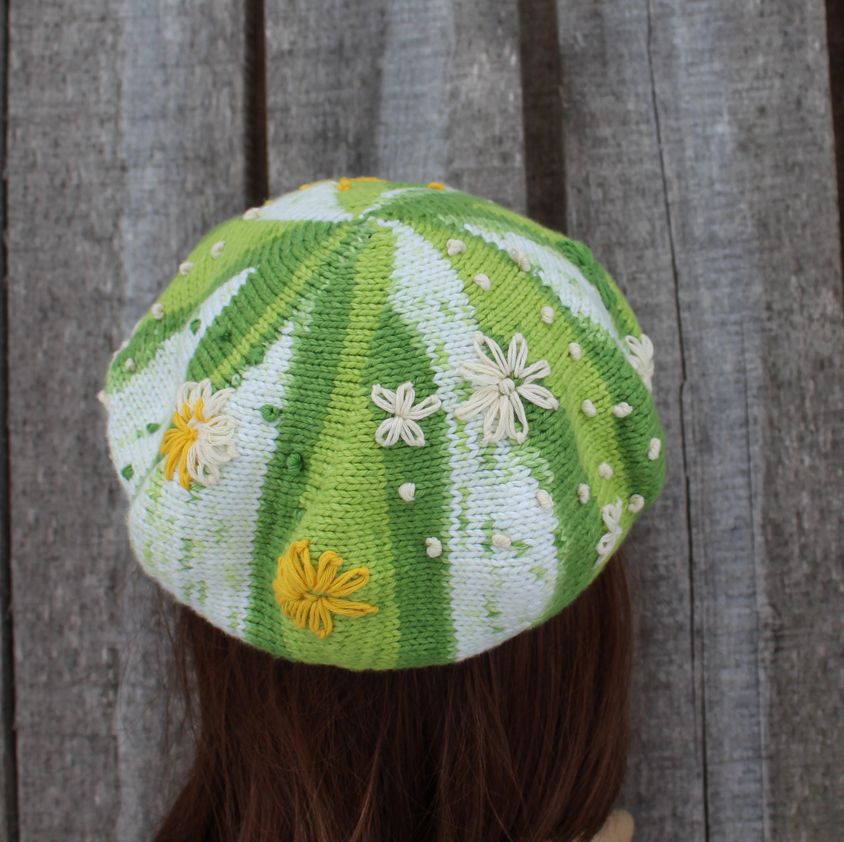 Green and white striped knit beret with floral patterns on a wooden background