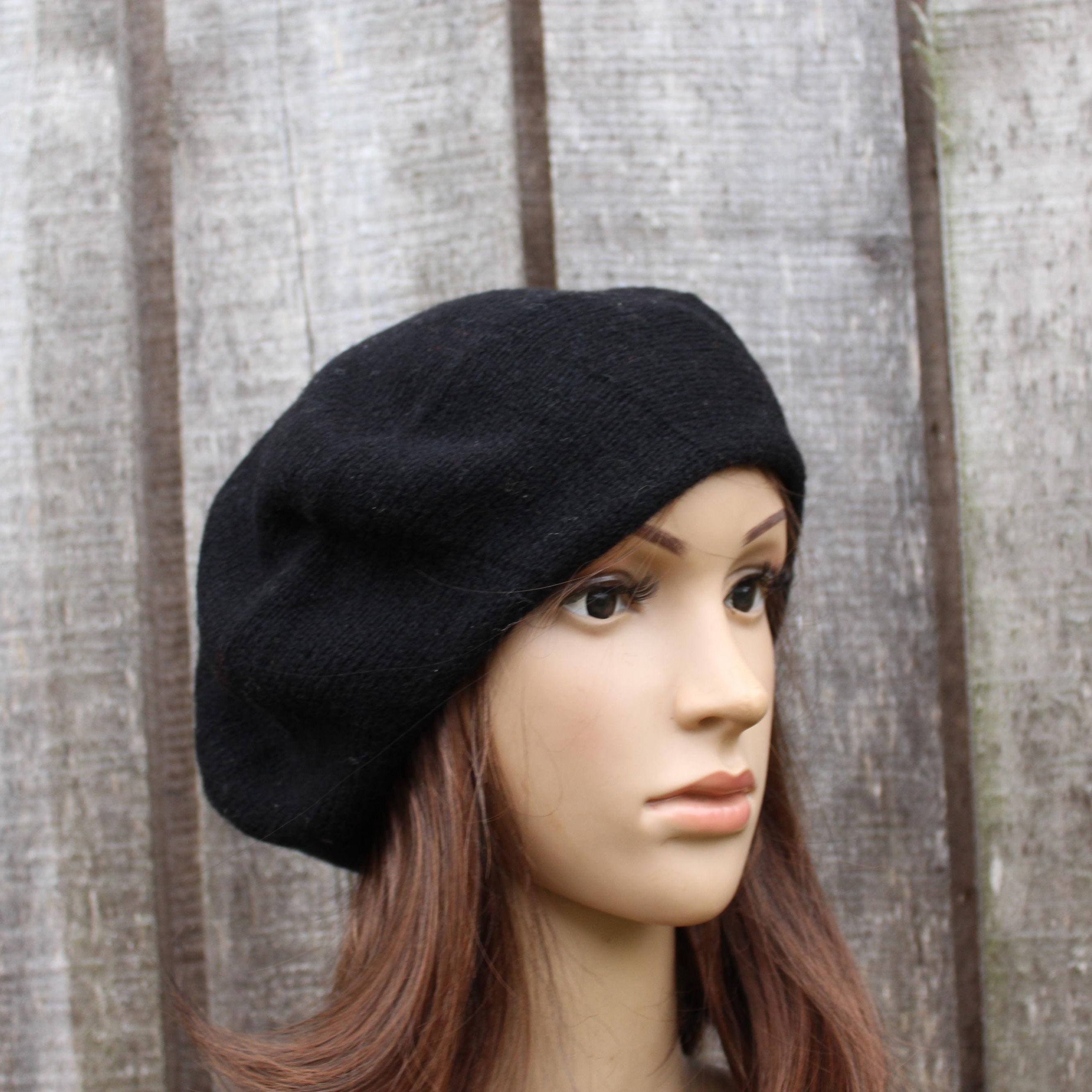 Black beret on a mannequin head against a wooden panel background