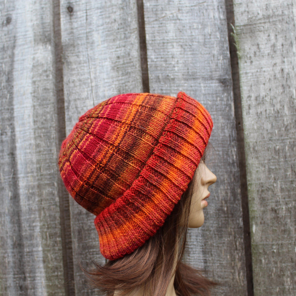 Person wearing a red and orange plaid knitted beanie against a wooden fence background