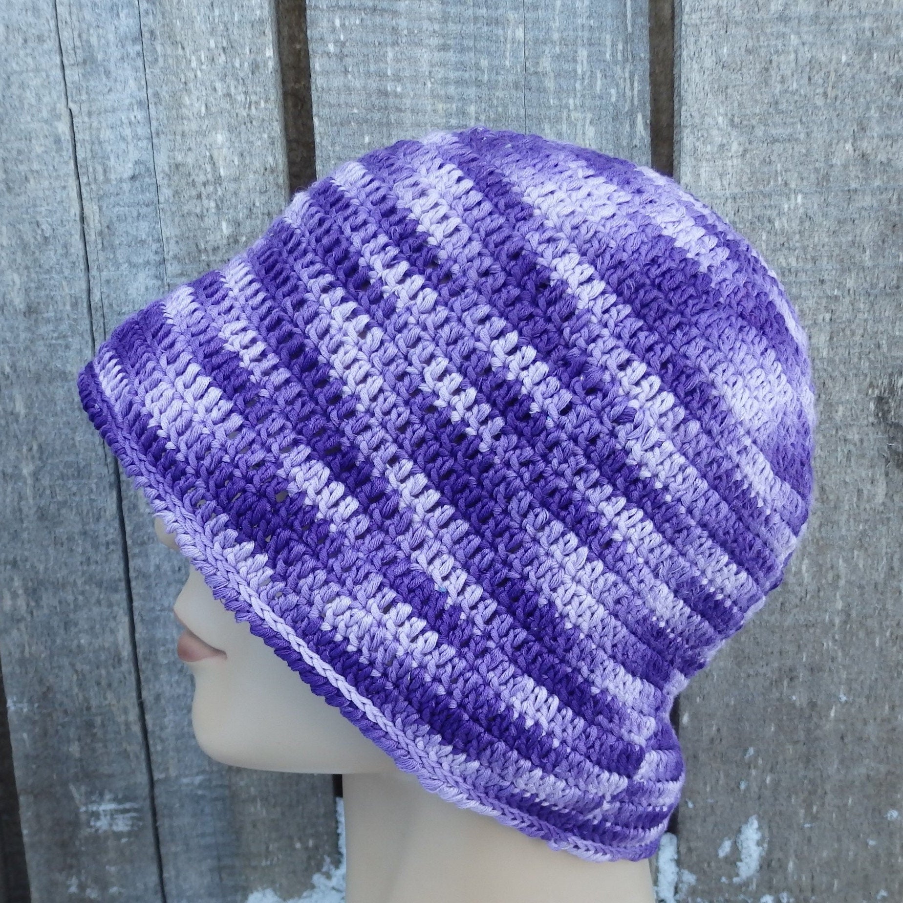 Purple and gray striped knit beanie on a mannequin head against a wooden background