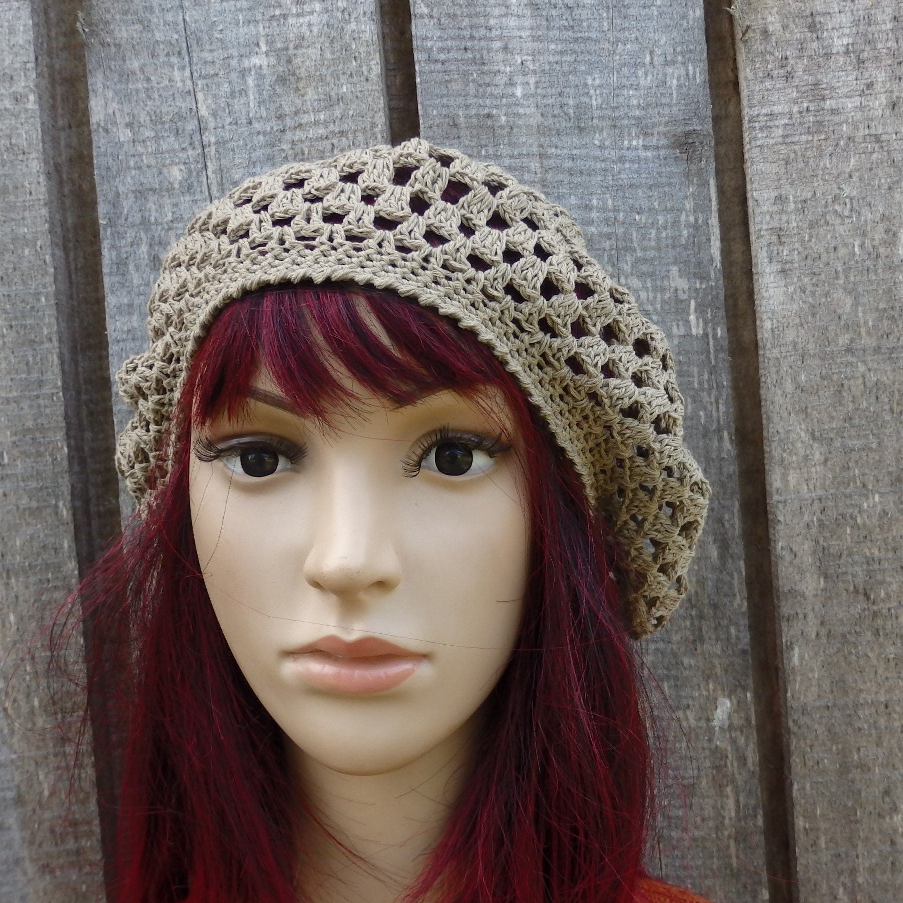 Mannequin head wearing a beige crochet hat against a wooden background