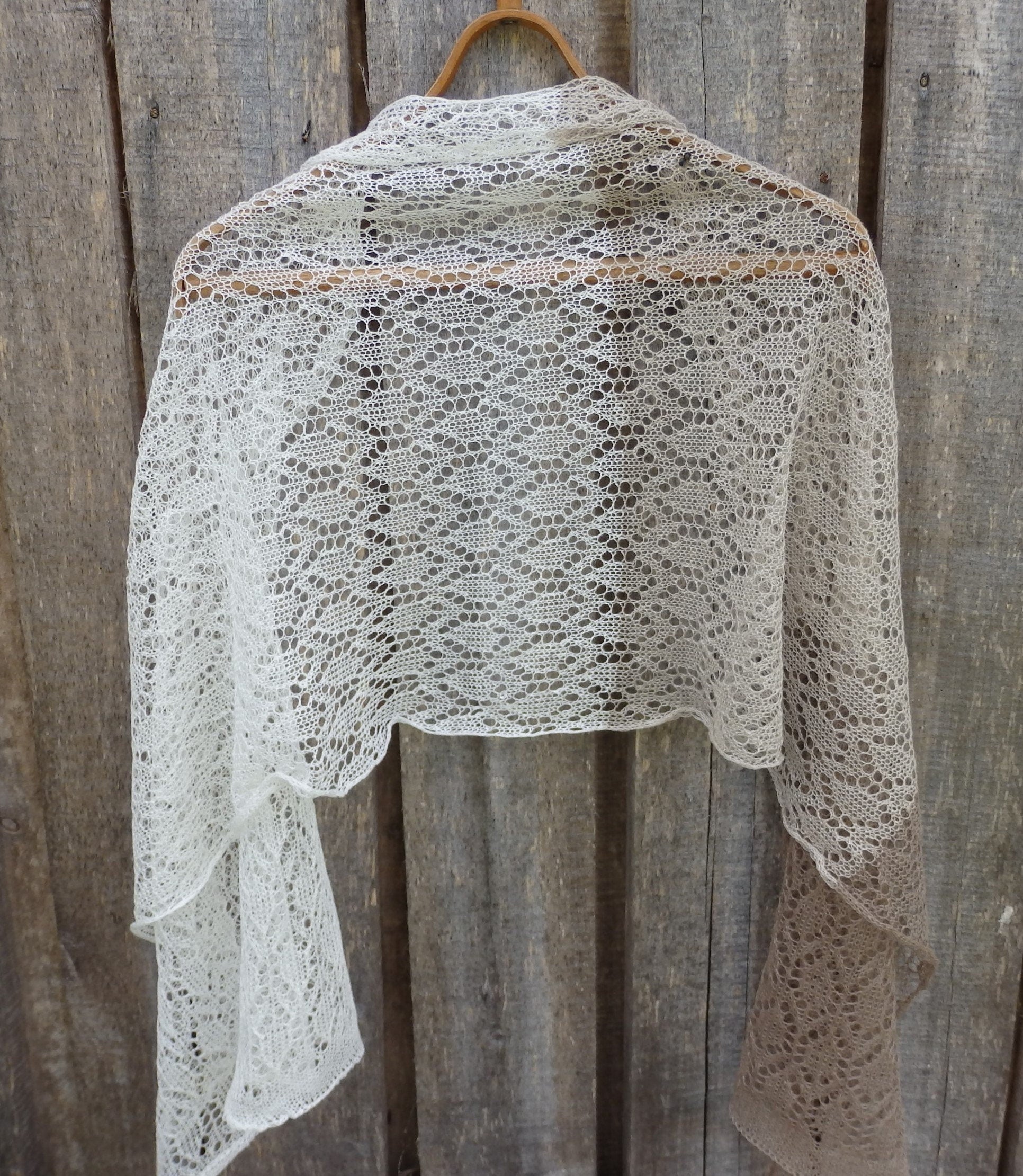 Knitted shawl hanging on a wooden hanger against a rustic wooden background
