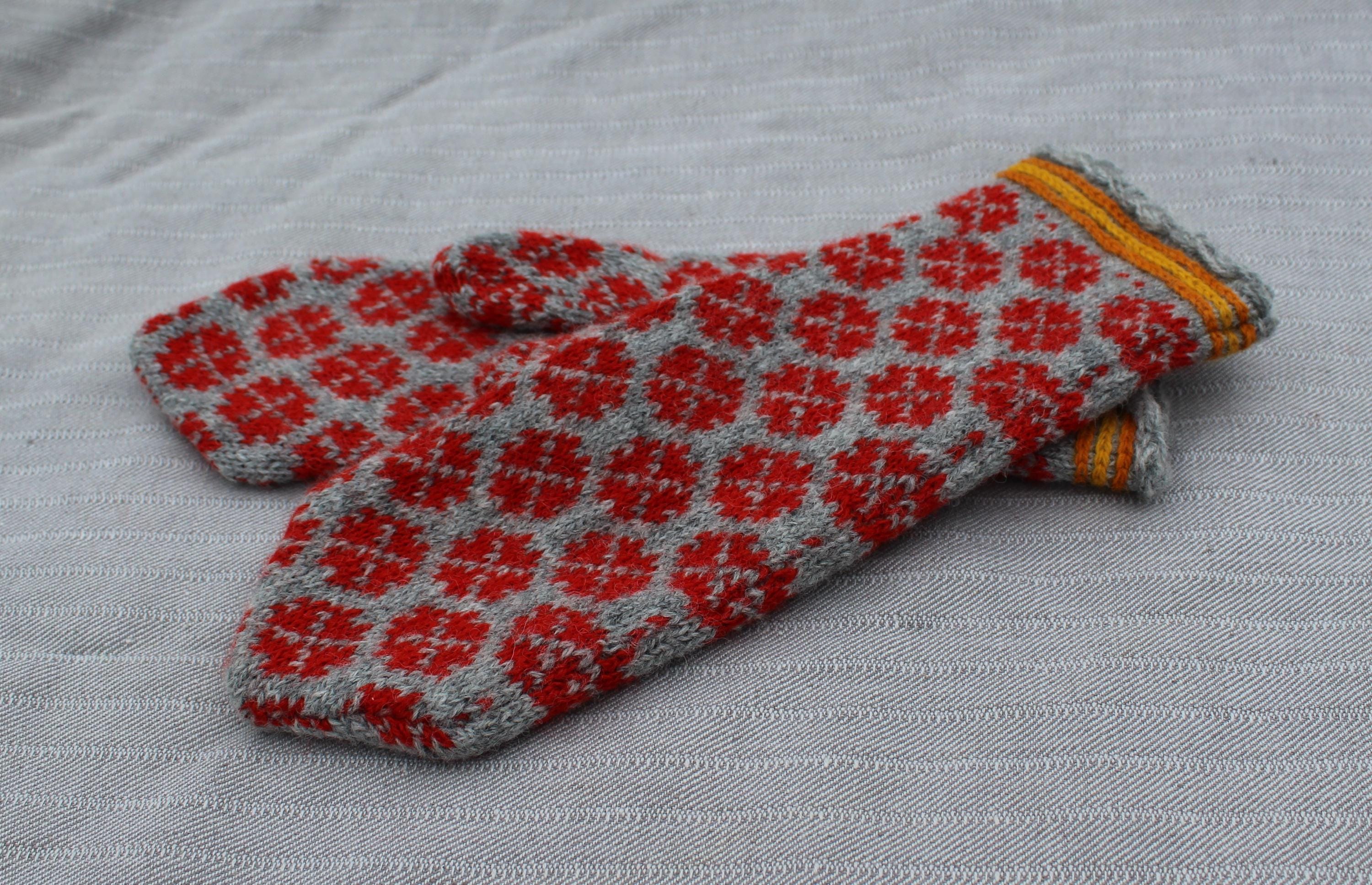 Pair of knitted mittens with red floral pattern on a light gray background