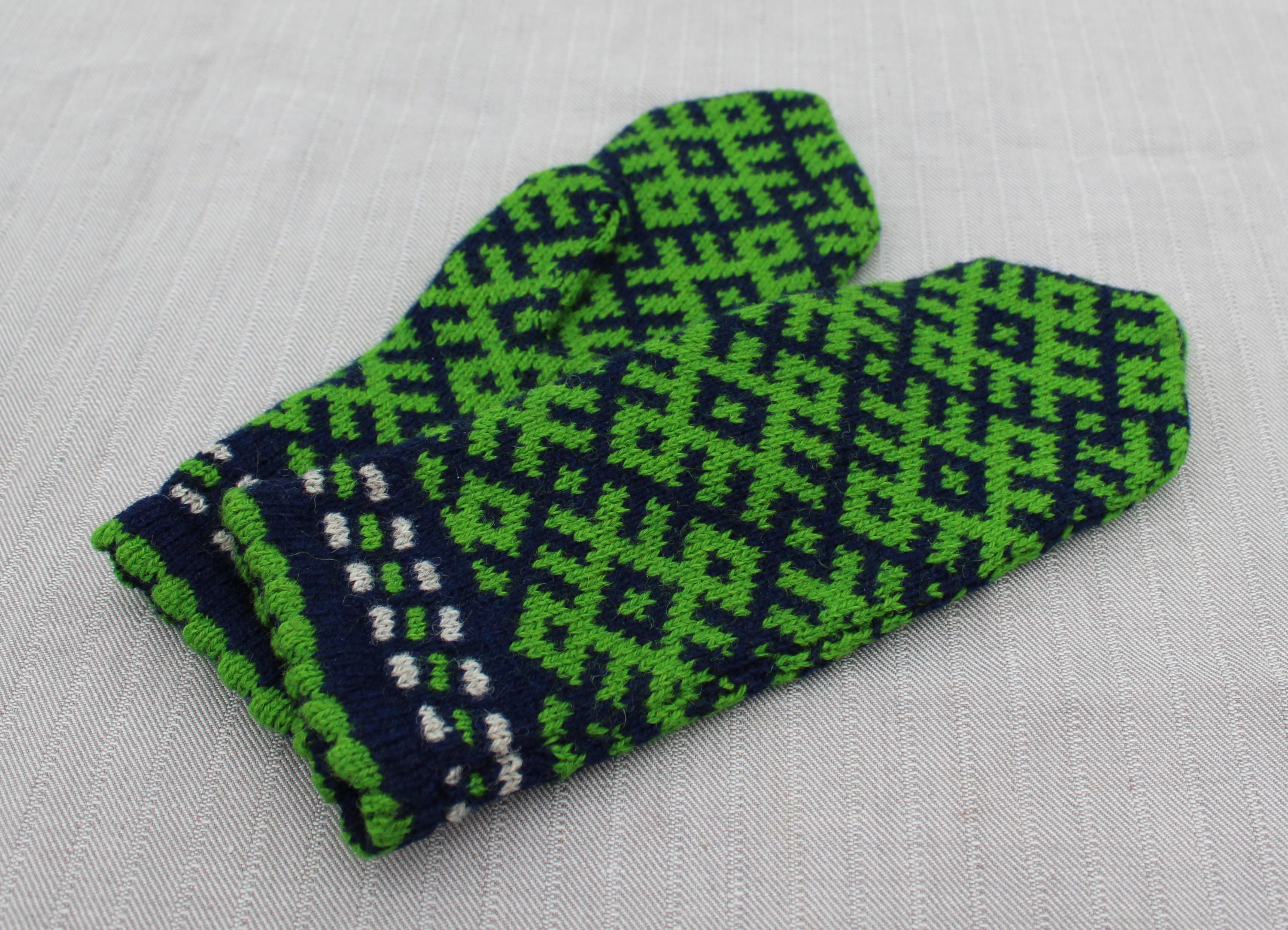 Green and navy patterned mittens on a light gray background
