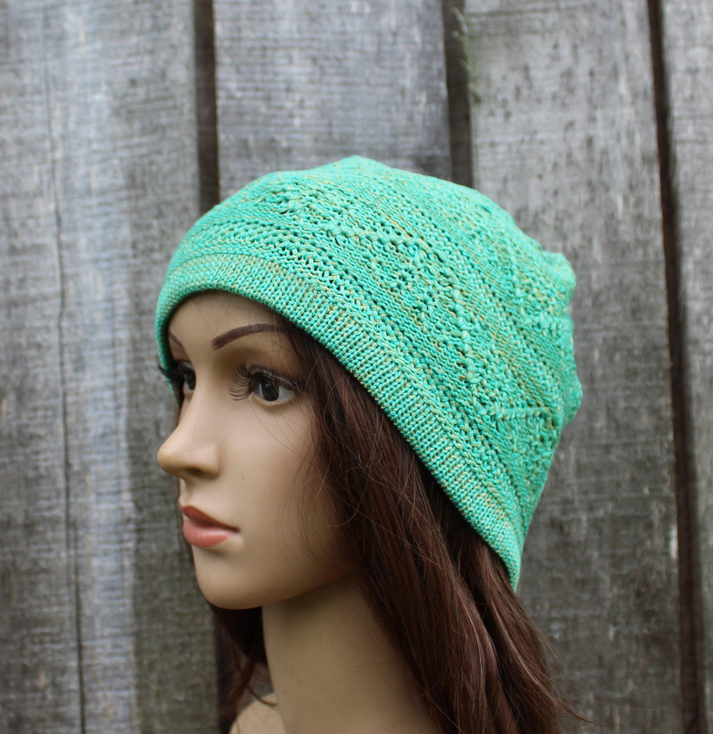 Mannequin head wearing a teal knitted hat against a wooden background