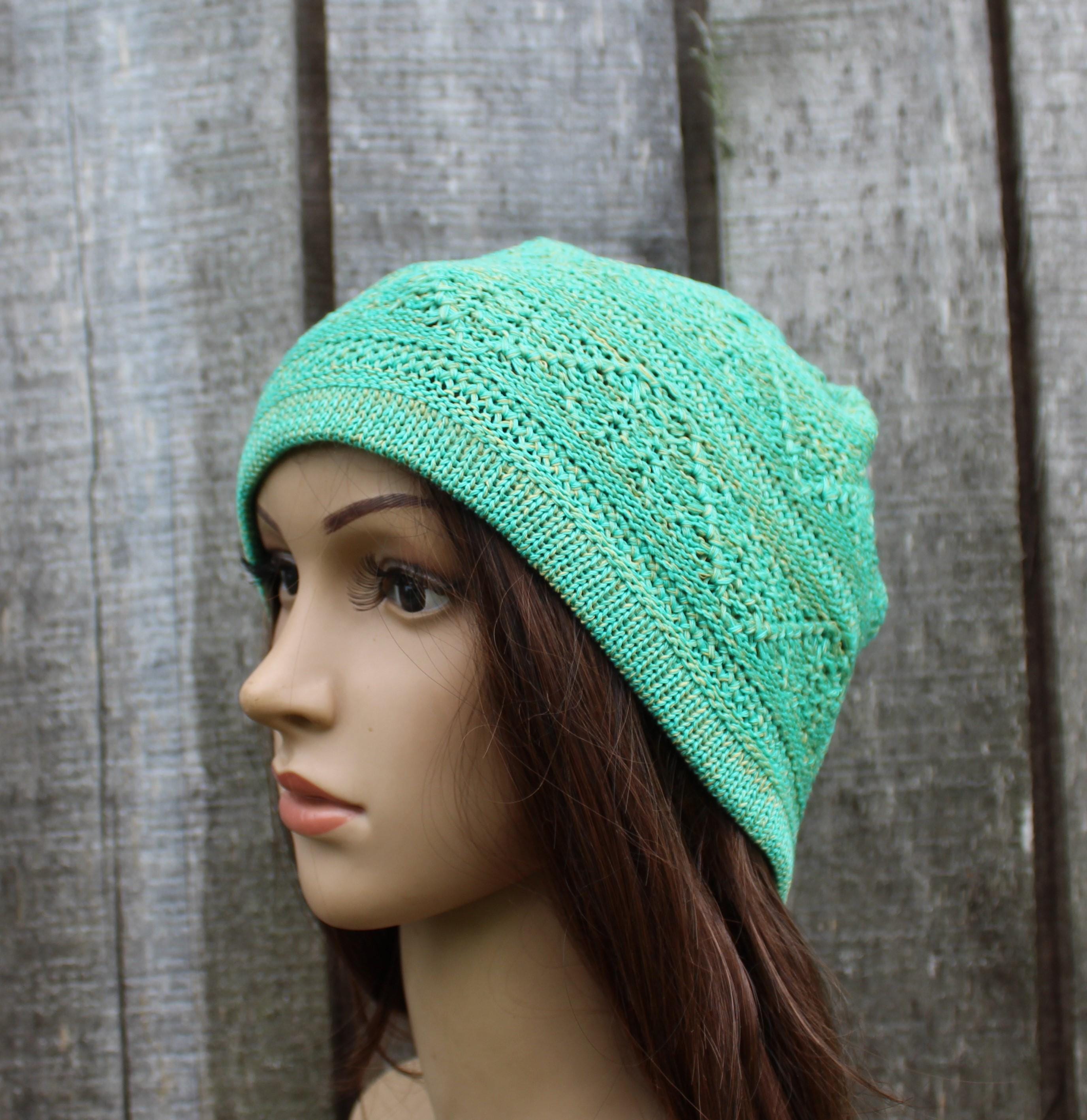 Mannequin head wearing a teal knitted hat against a wooden background