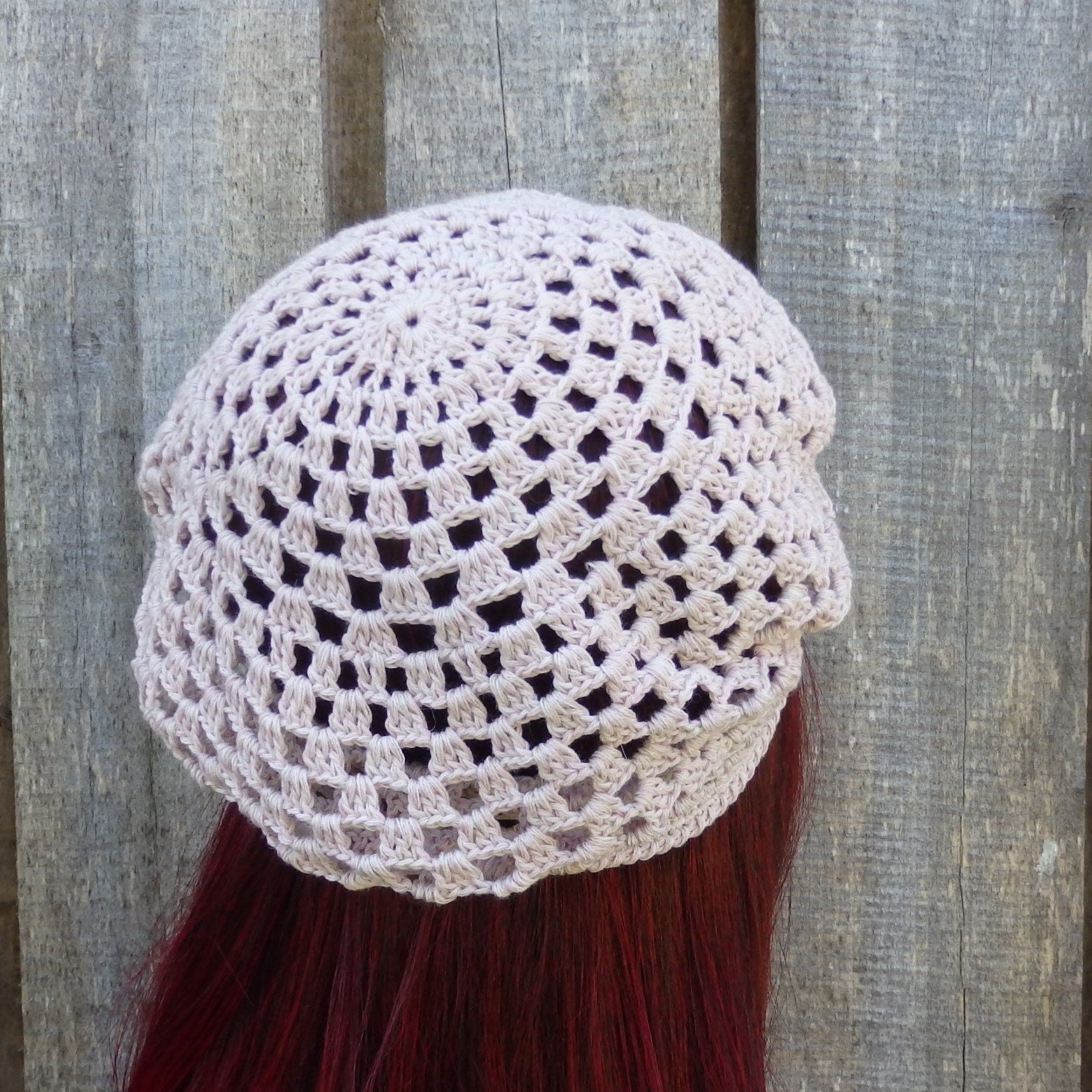 Crocheted beige hat on a person with red hair against a wooden background