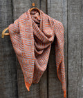 Knitted scarf with orange and white pattern draped over a wooden hanger against a wooden background