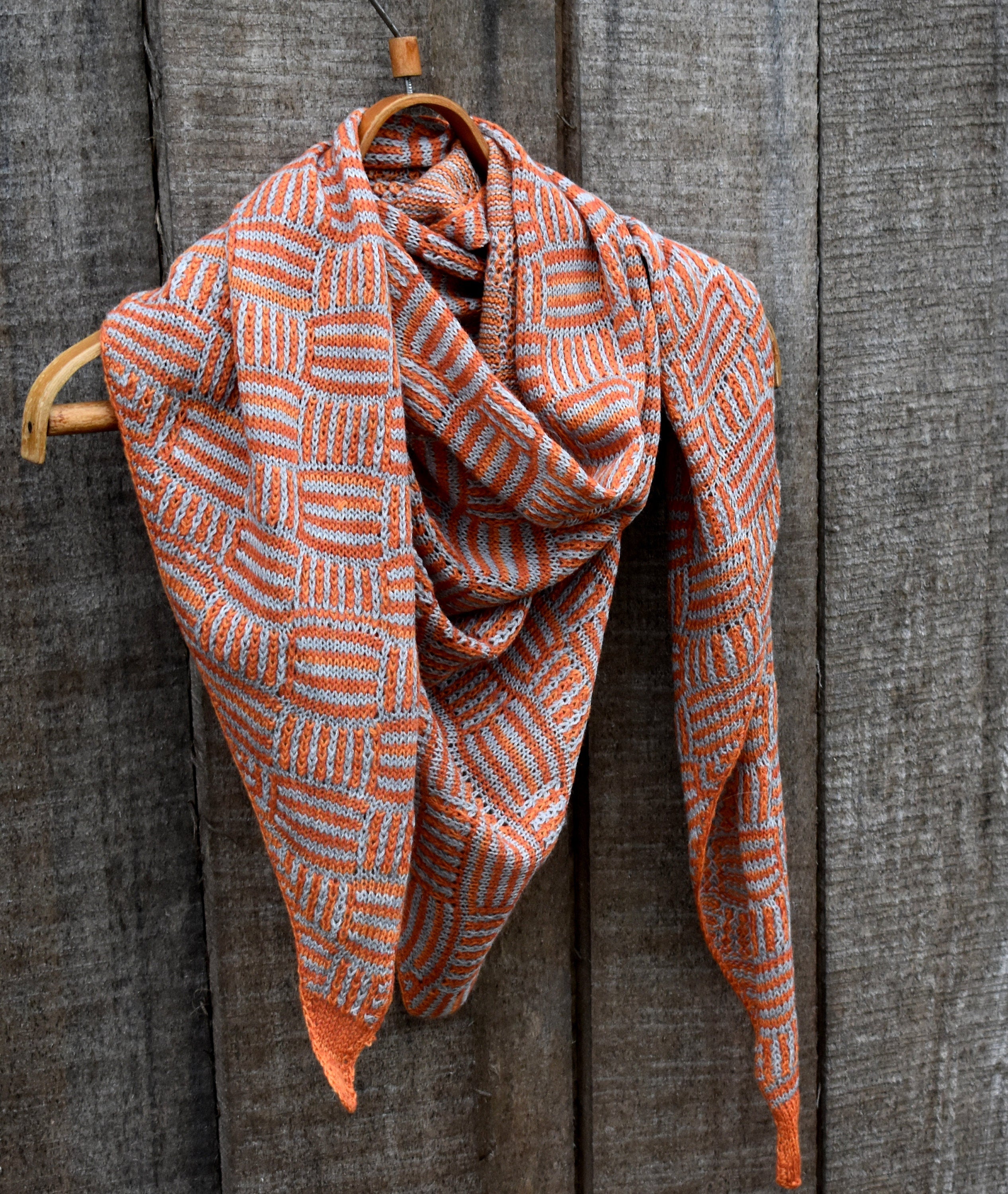 Knitted scarf with orange and white pattern draped over a wooden hanger against a wooden background