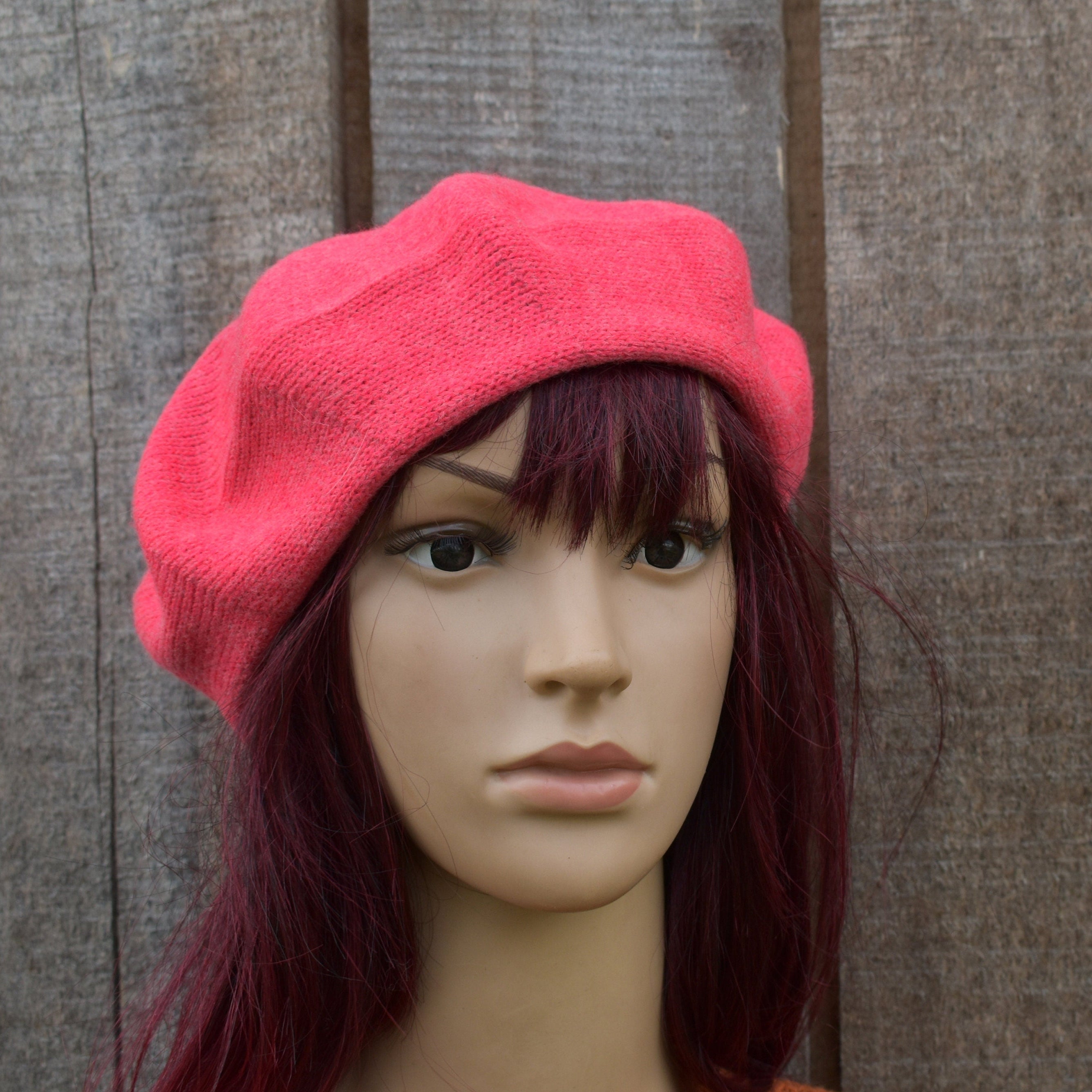 Mannequin head wearing a bright pink beret against a wooden panel background
