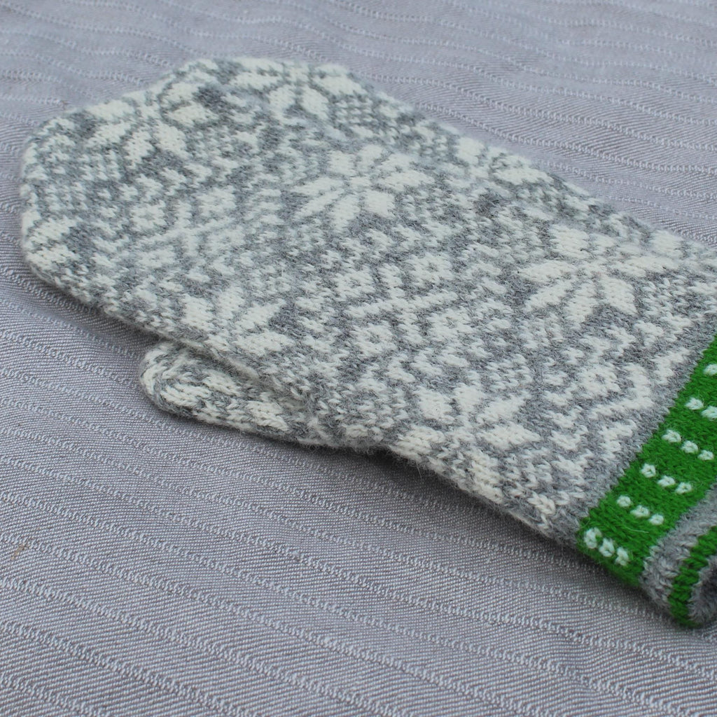 Knitted gray and green mittens on a gray fabric background