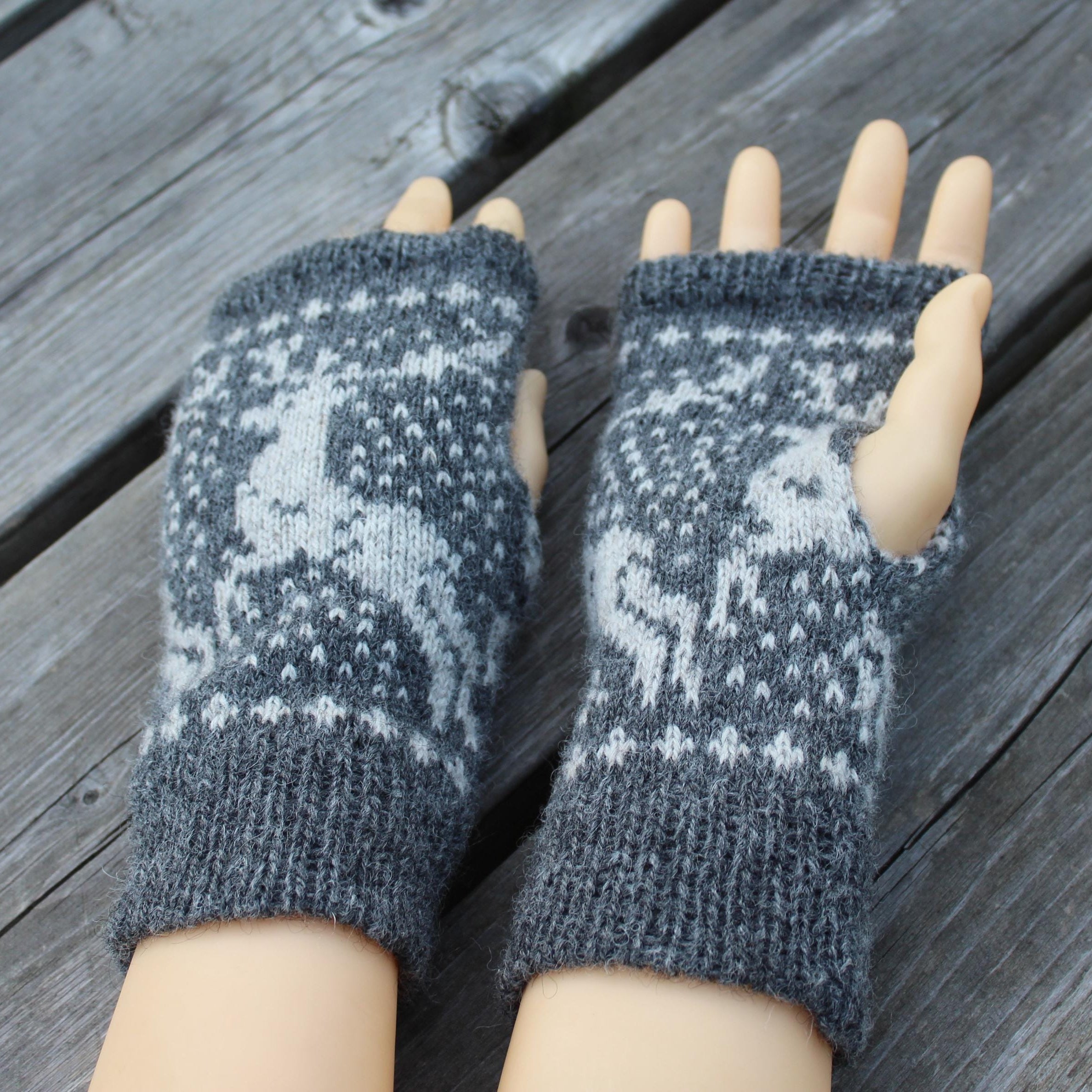 Pair of gray knit fingerless gloves with a pattern on a wooden surface
