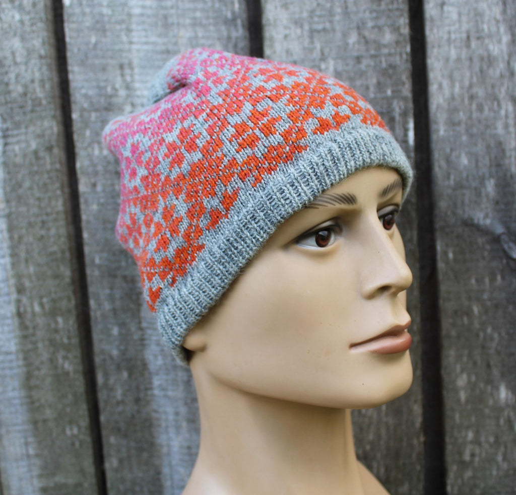 Mannequin head wearing a gray and pink patterned knit hat against a wooden fence background