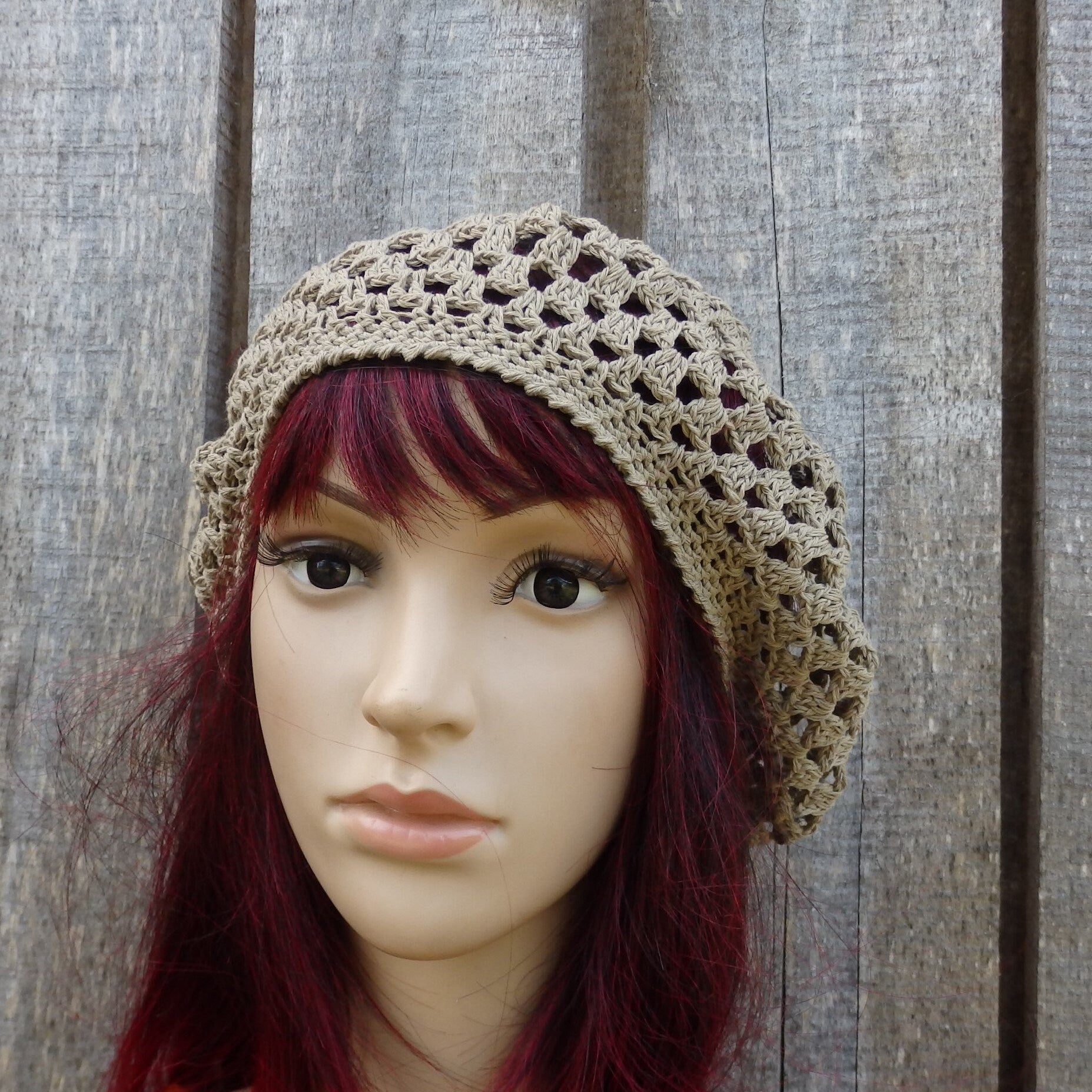 Mannequin head wearing a beige crochet hat against a wooden background