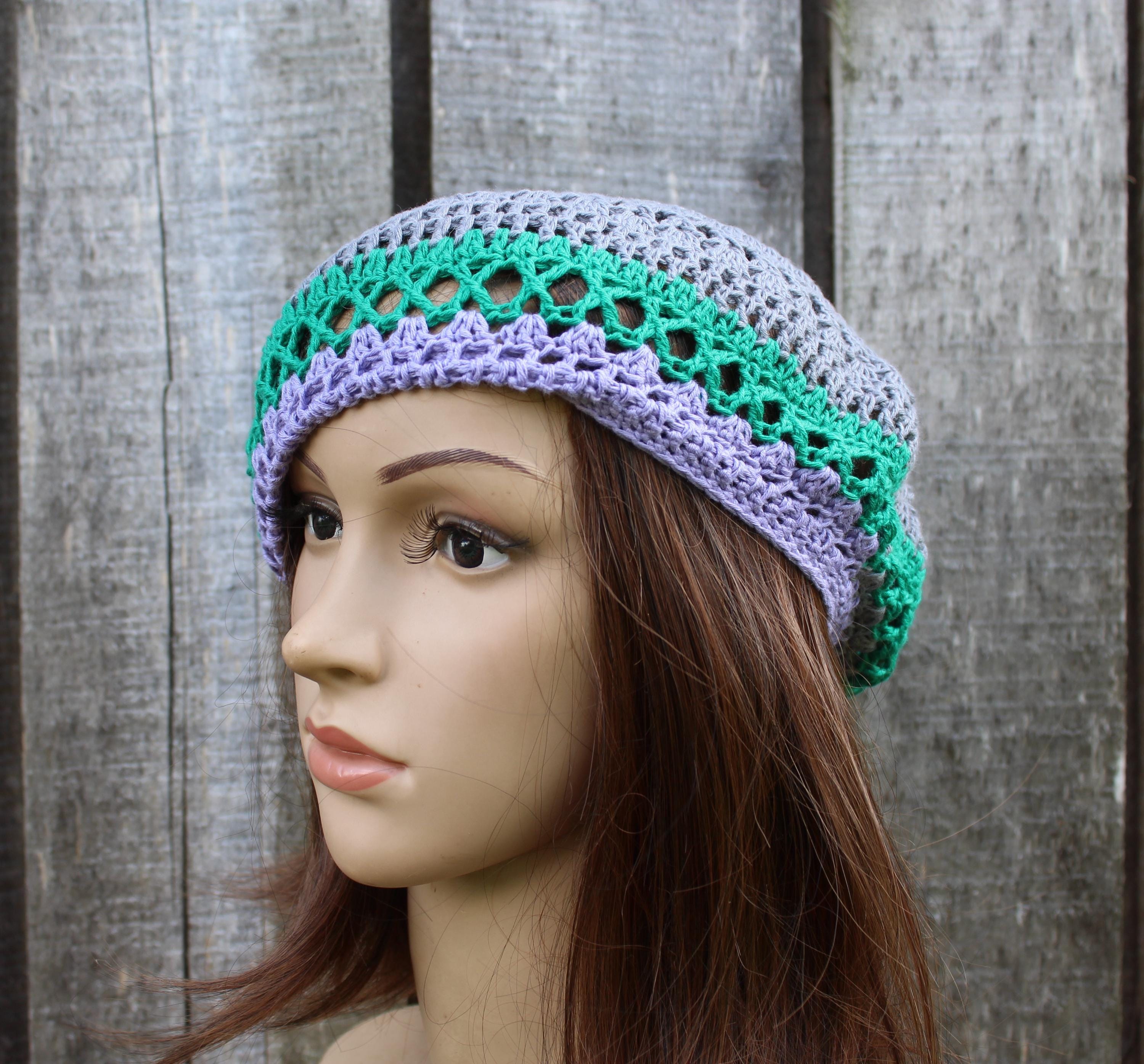 Mannequin head wearing a crocheted hat with green and purple patterns against a wooden background