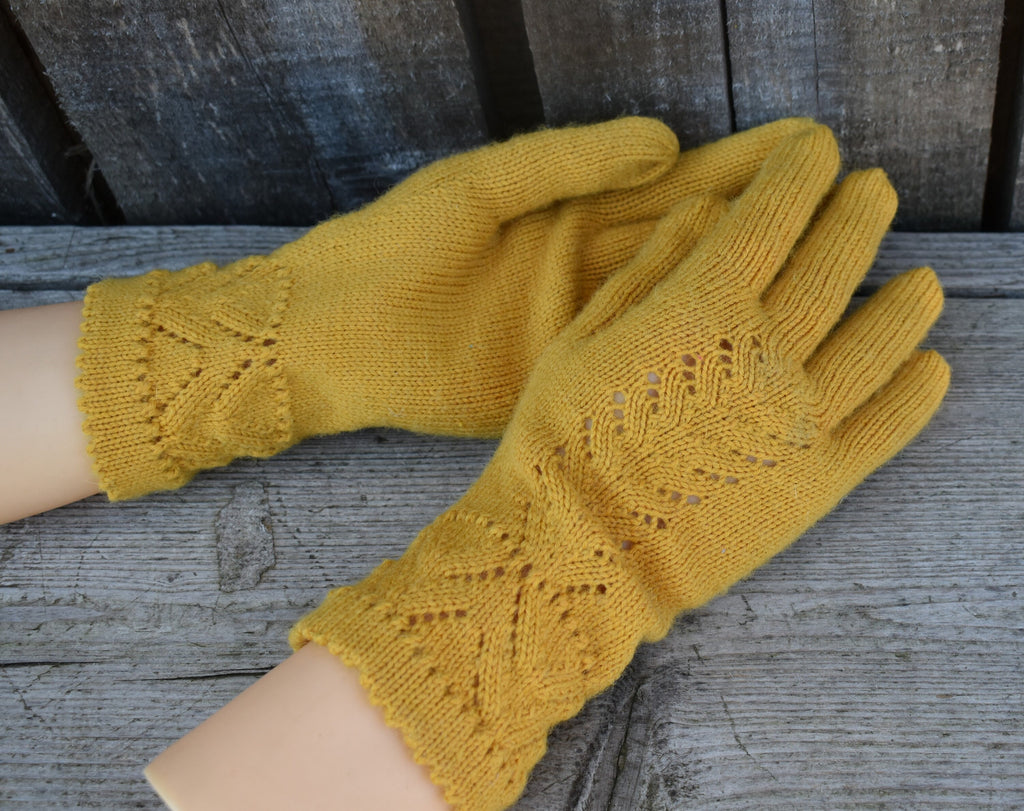 Pair of yellow knitted gloves with lace pattern on a wooden surface