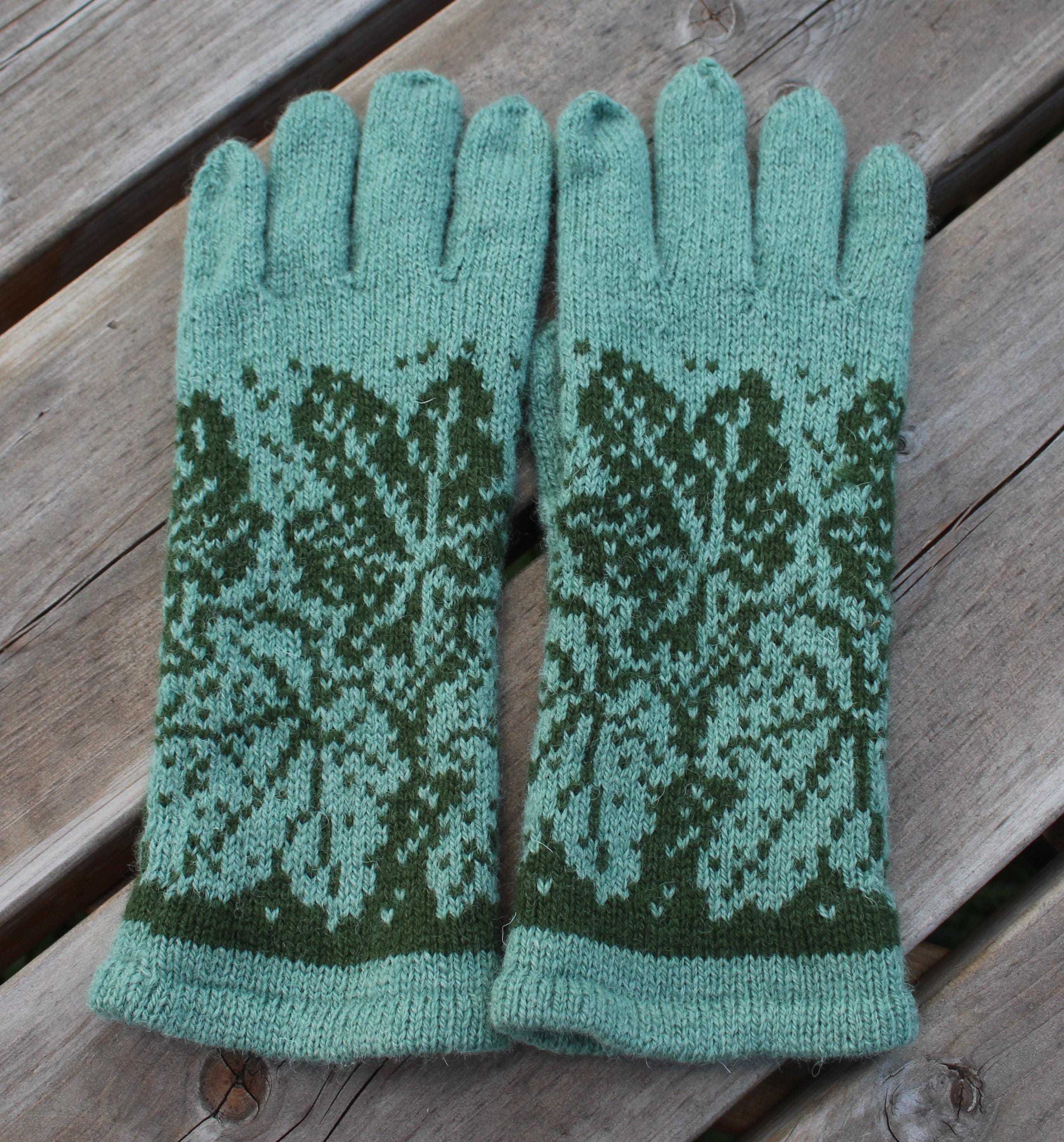 Pair of green knitted gloves with a pattern on a wooden surface