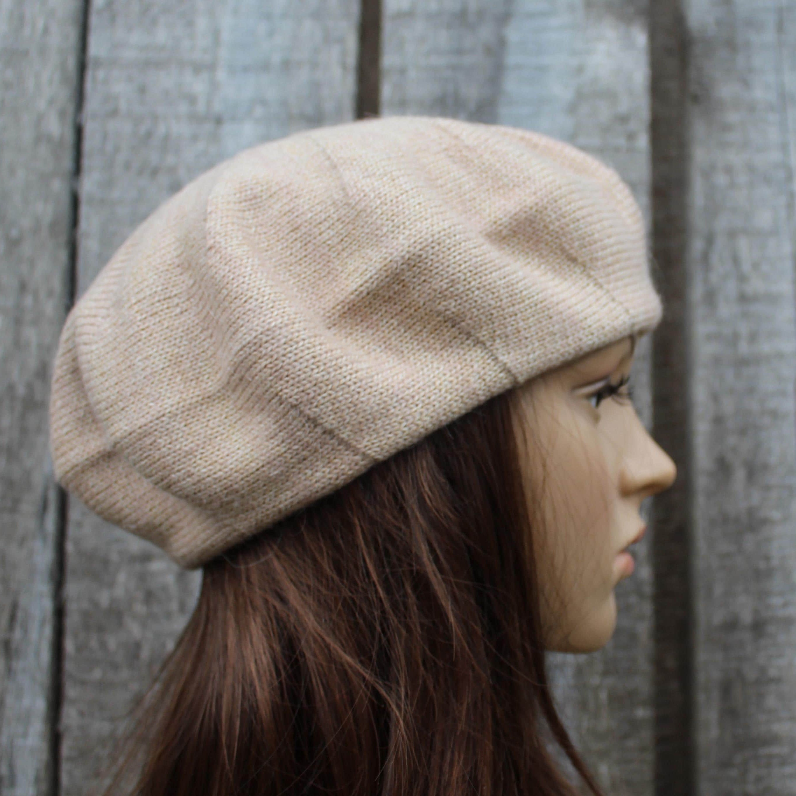 Beige knit beret worn by a mannequin against a wooden fence background