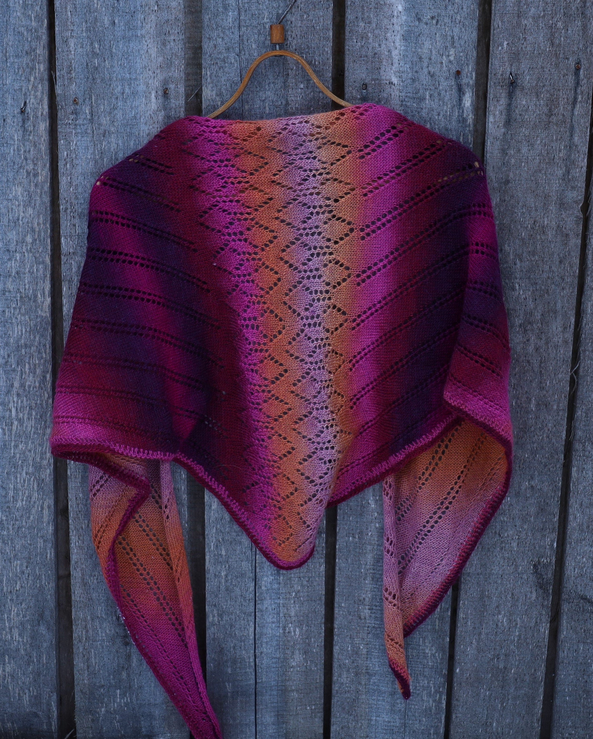 Purple and pink patterned shawl on a wooden hanger against a wooden background