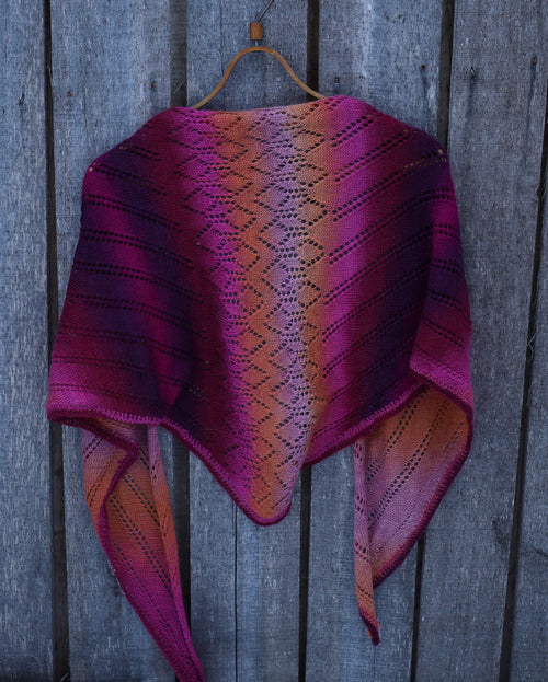 Purple and pink patterned shawl on a wooden hanger against a wooden background