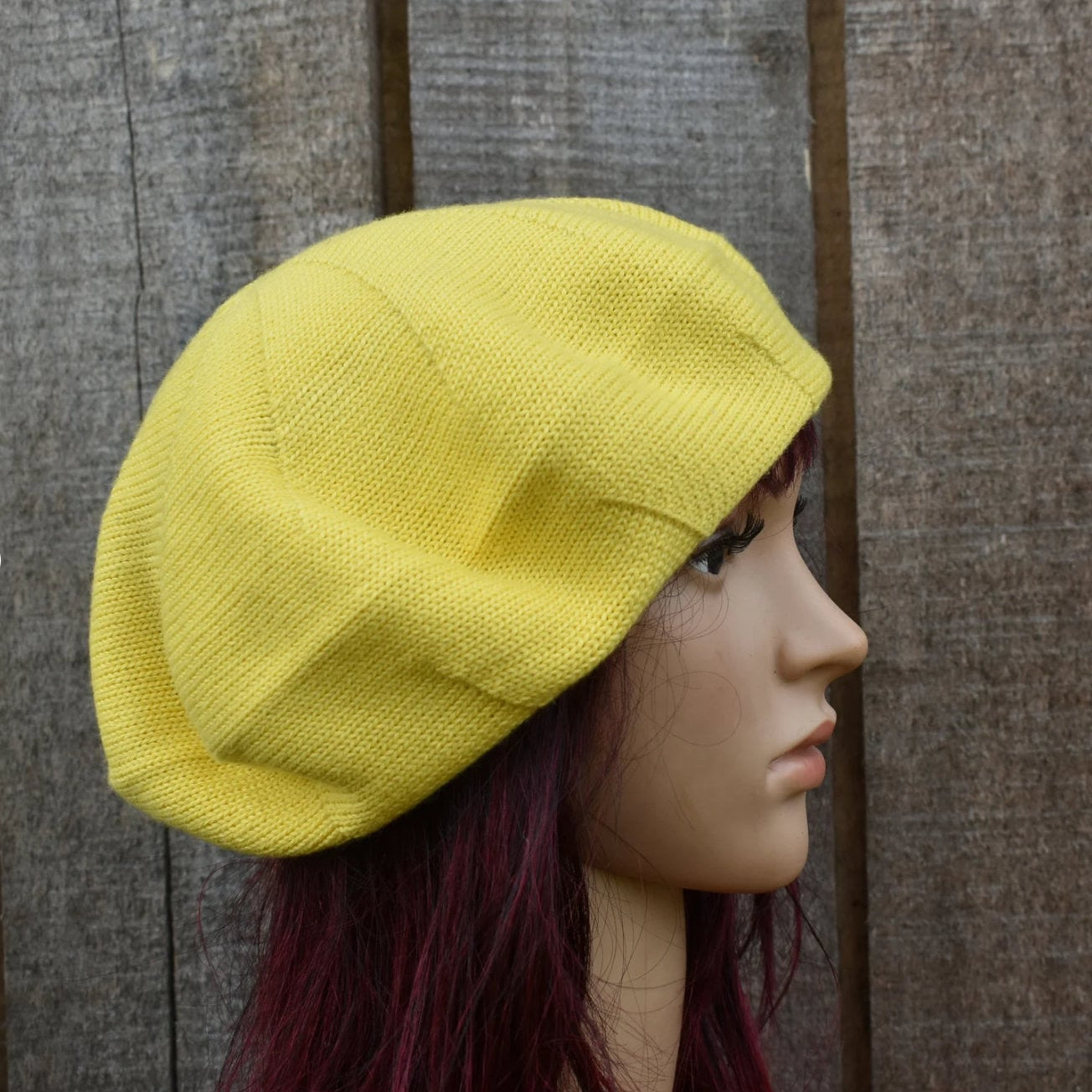 Yellow knitted beret on a mannequin head against a wooden background