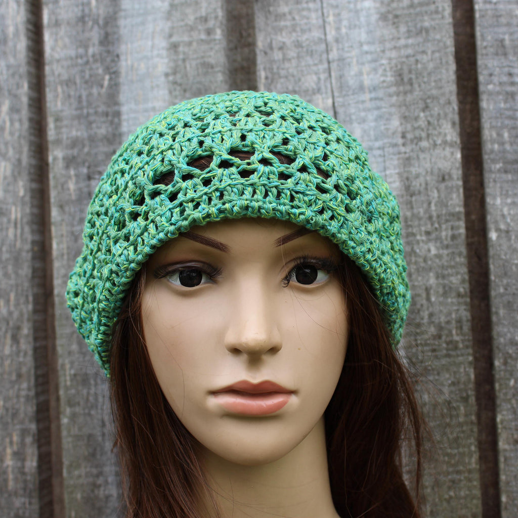 Green crocheted hat on a mannequin head against a wooden background