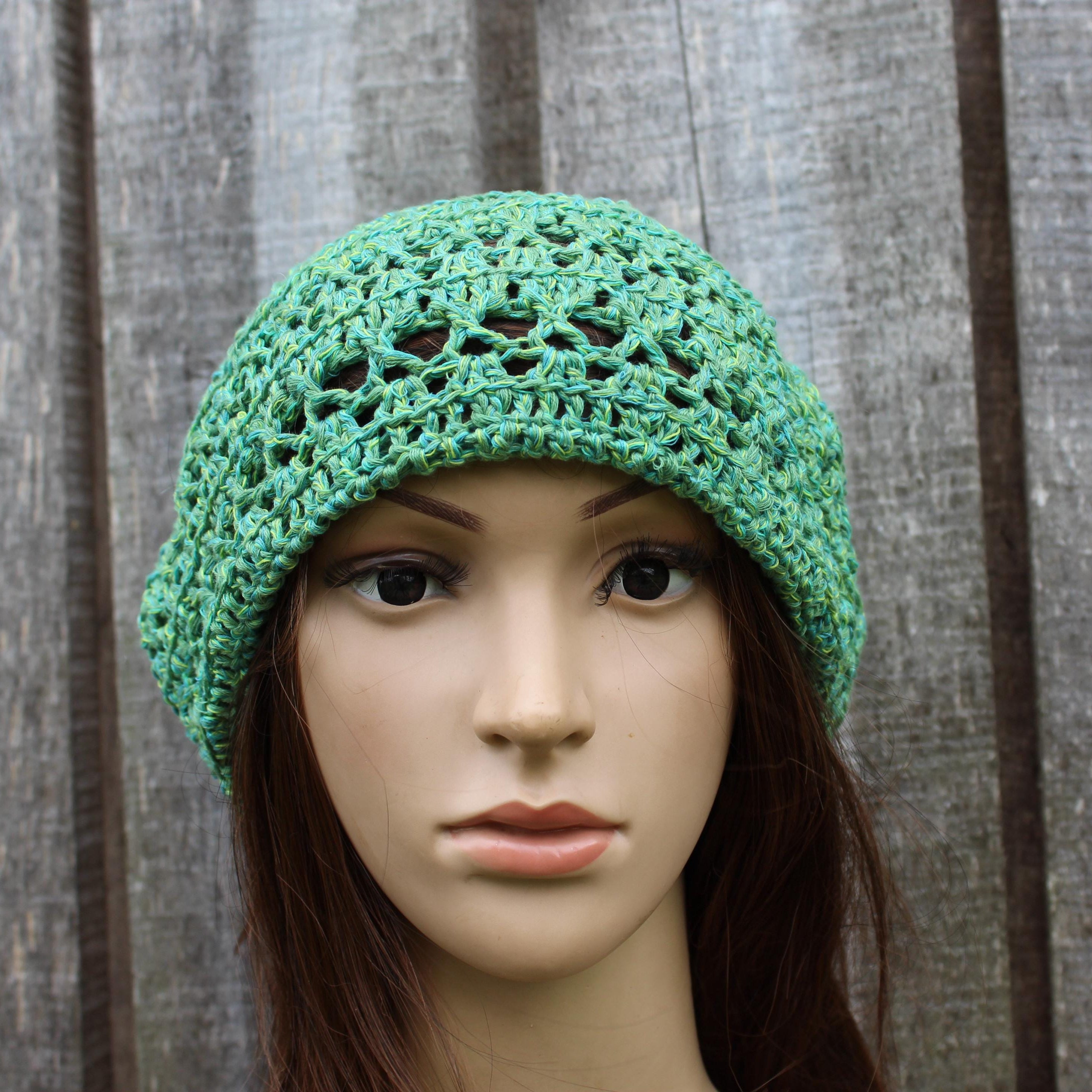 Green crocheted hat on a mannequin head against a wooden background
