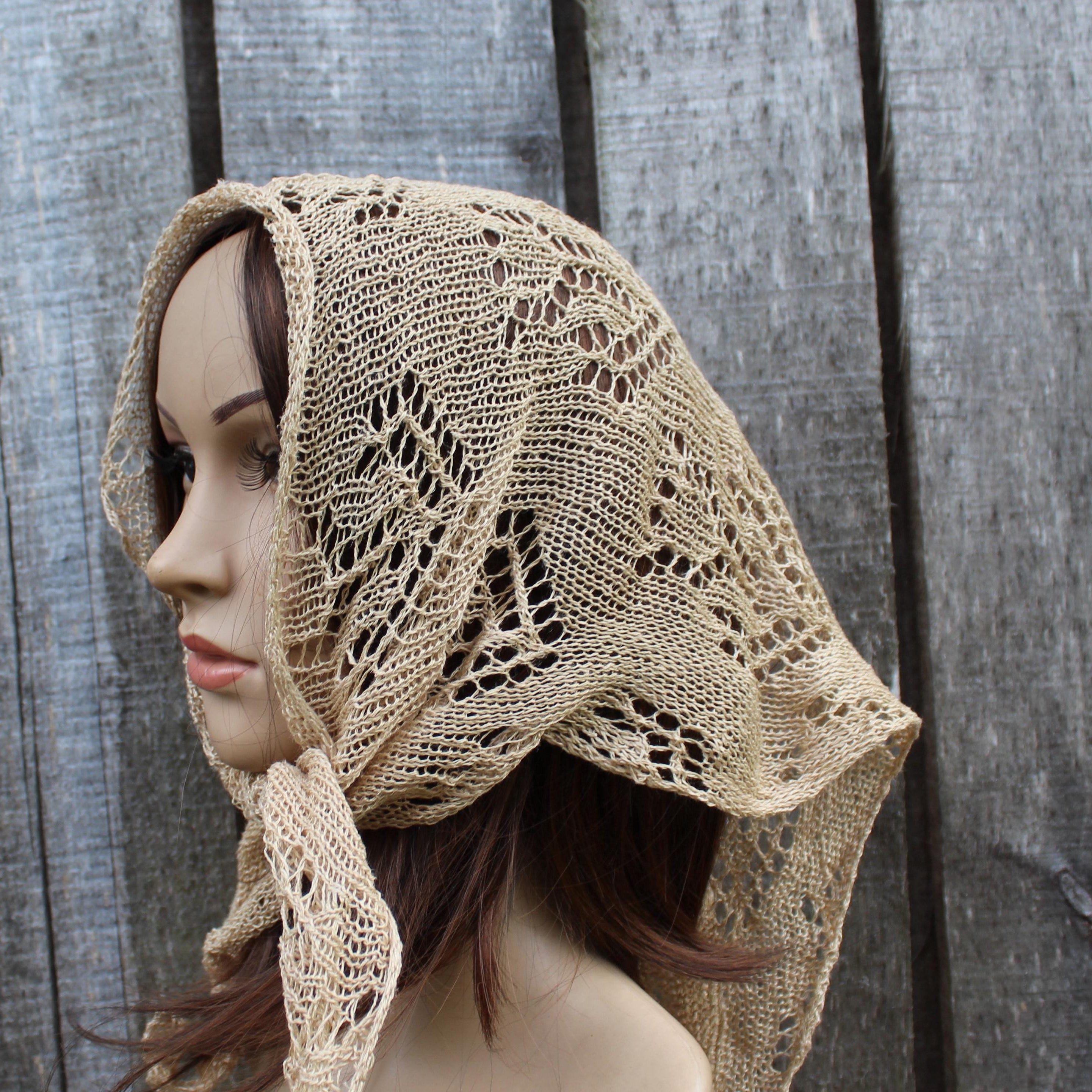 Mannequin head wearing a beige knitted shawl against a wooden background
