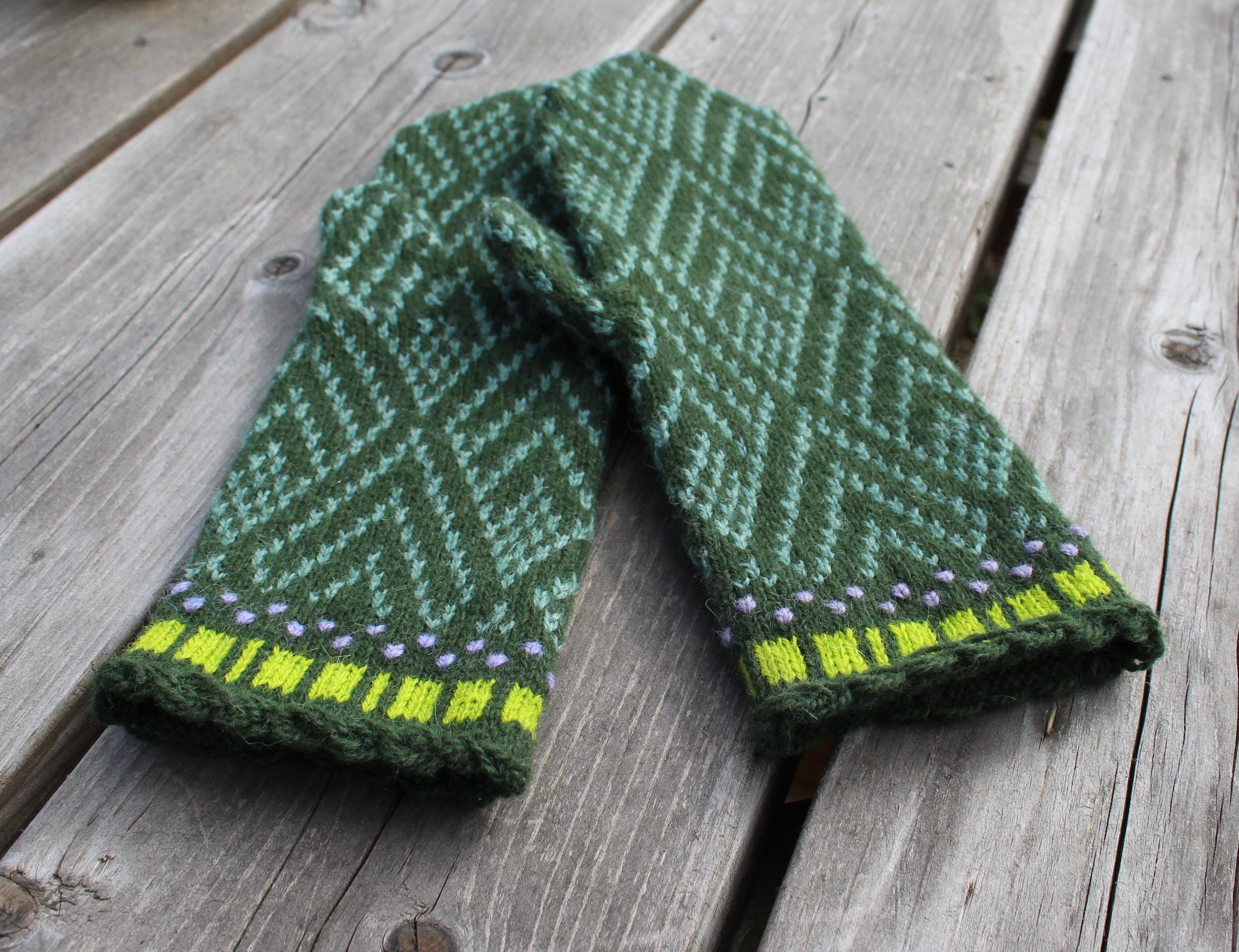 Green knitted gloves with a pattern on a wooden surface