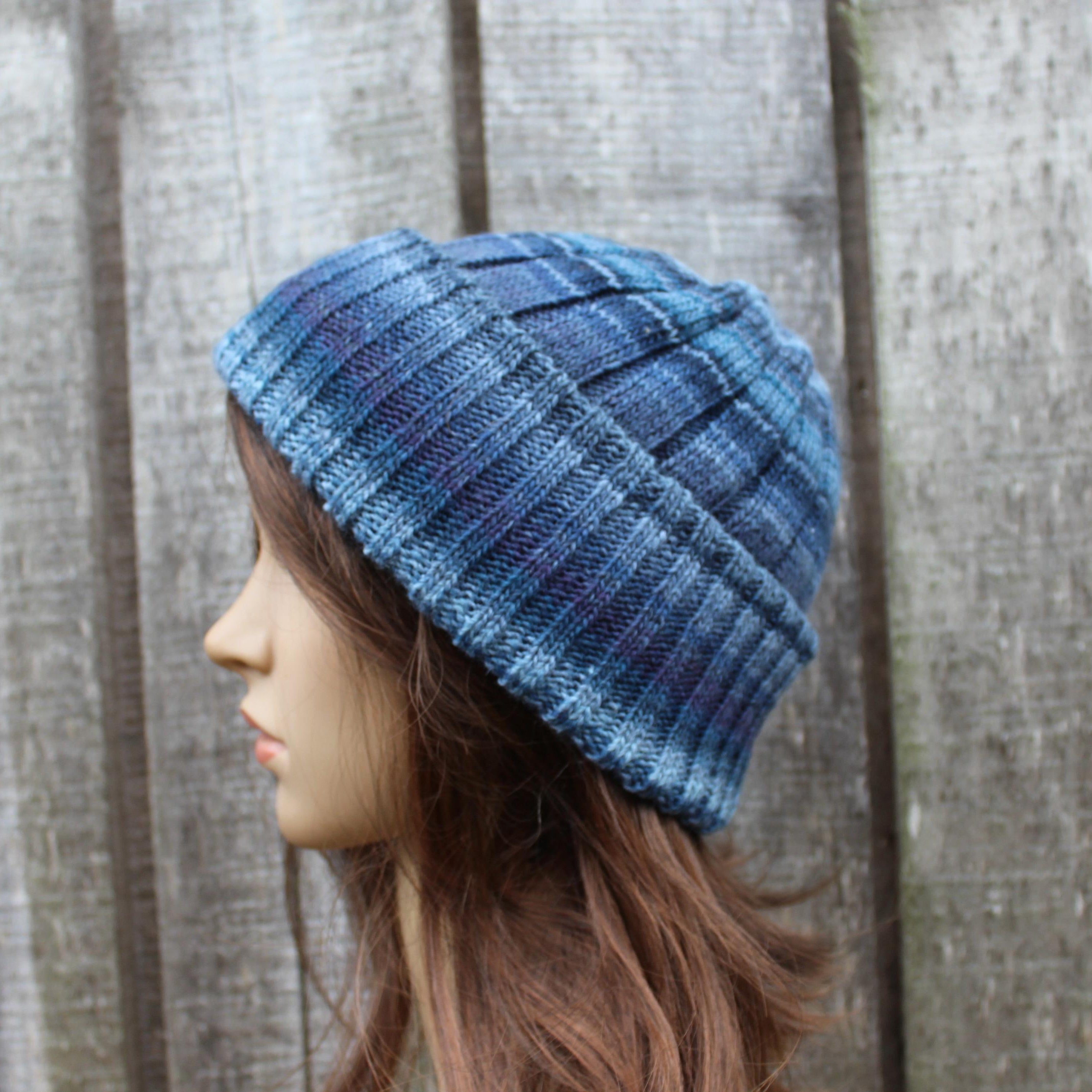 Blue knitted beanie worn by a mannequin against a wooden fence background