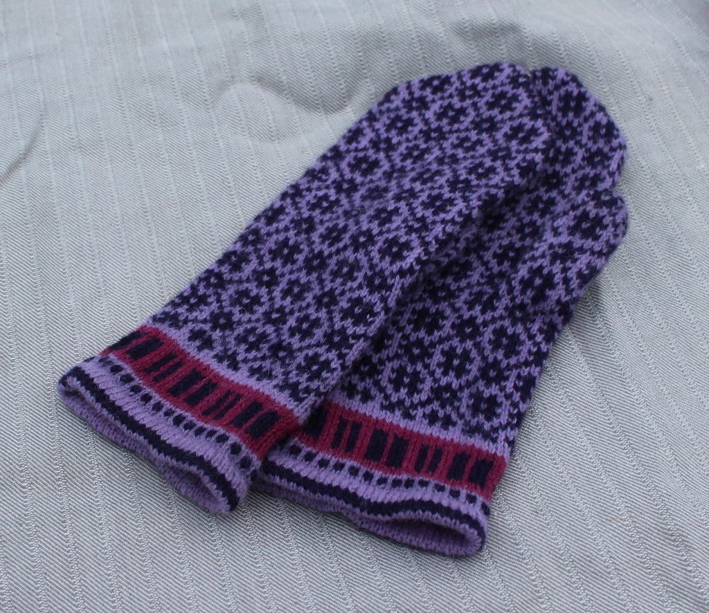 Pair of purple knitted mittens with a pattern on a gray fabric background