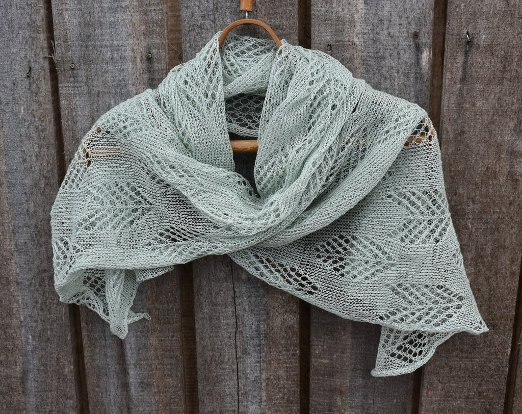Light green knitted shawl on a wooden hanger against a wooden background