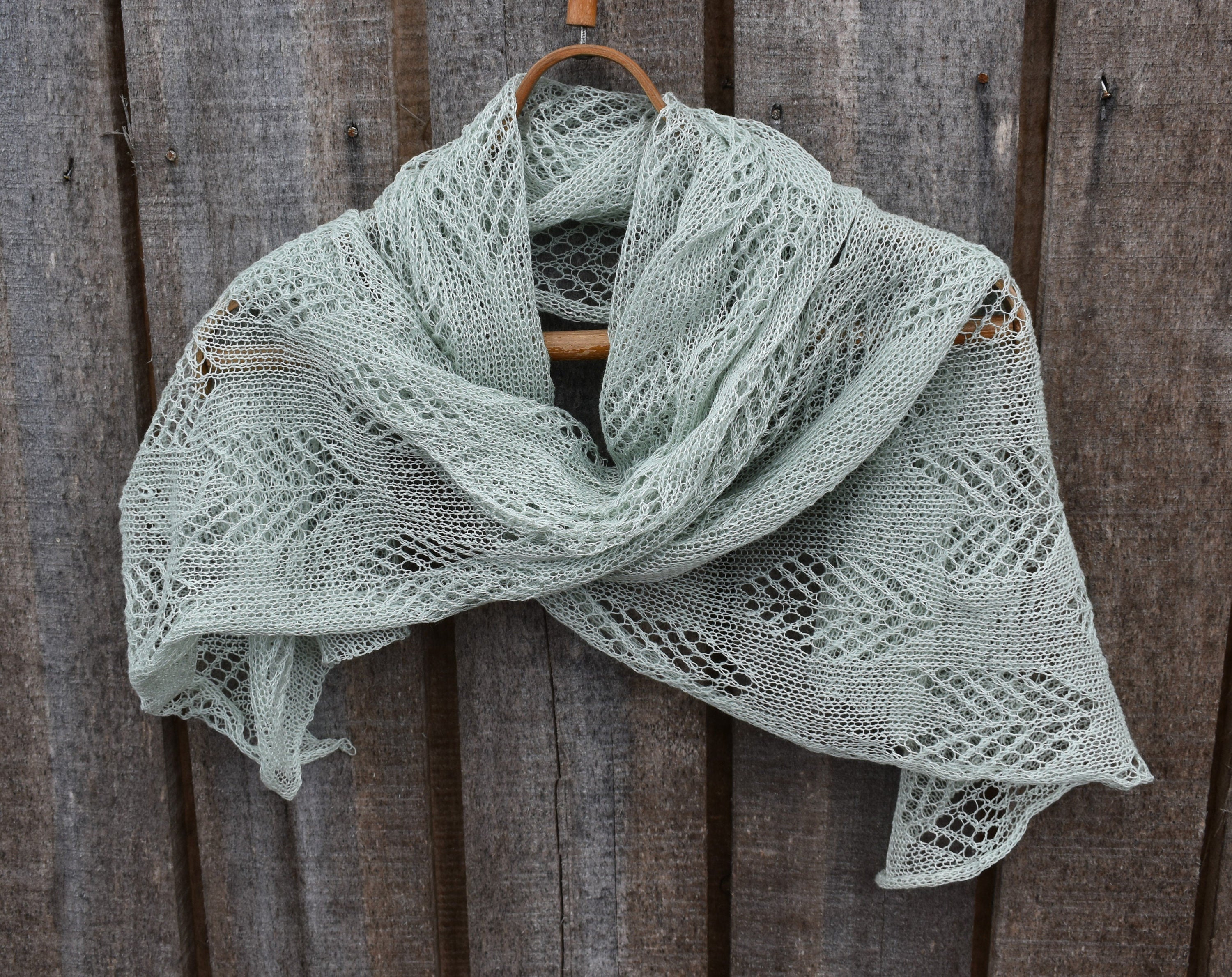Light green knitted shawl on a wooden hanger against a wooden background
