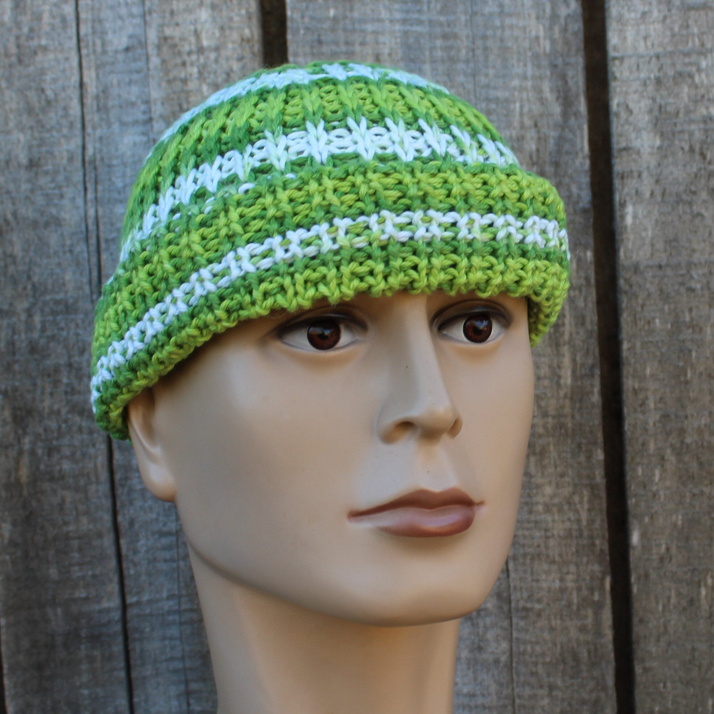 Green and white striped knitted hat on a mannequin head against a wooden background