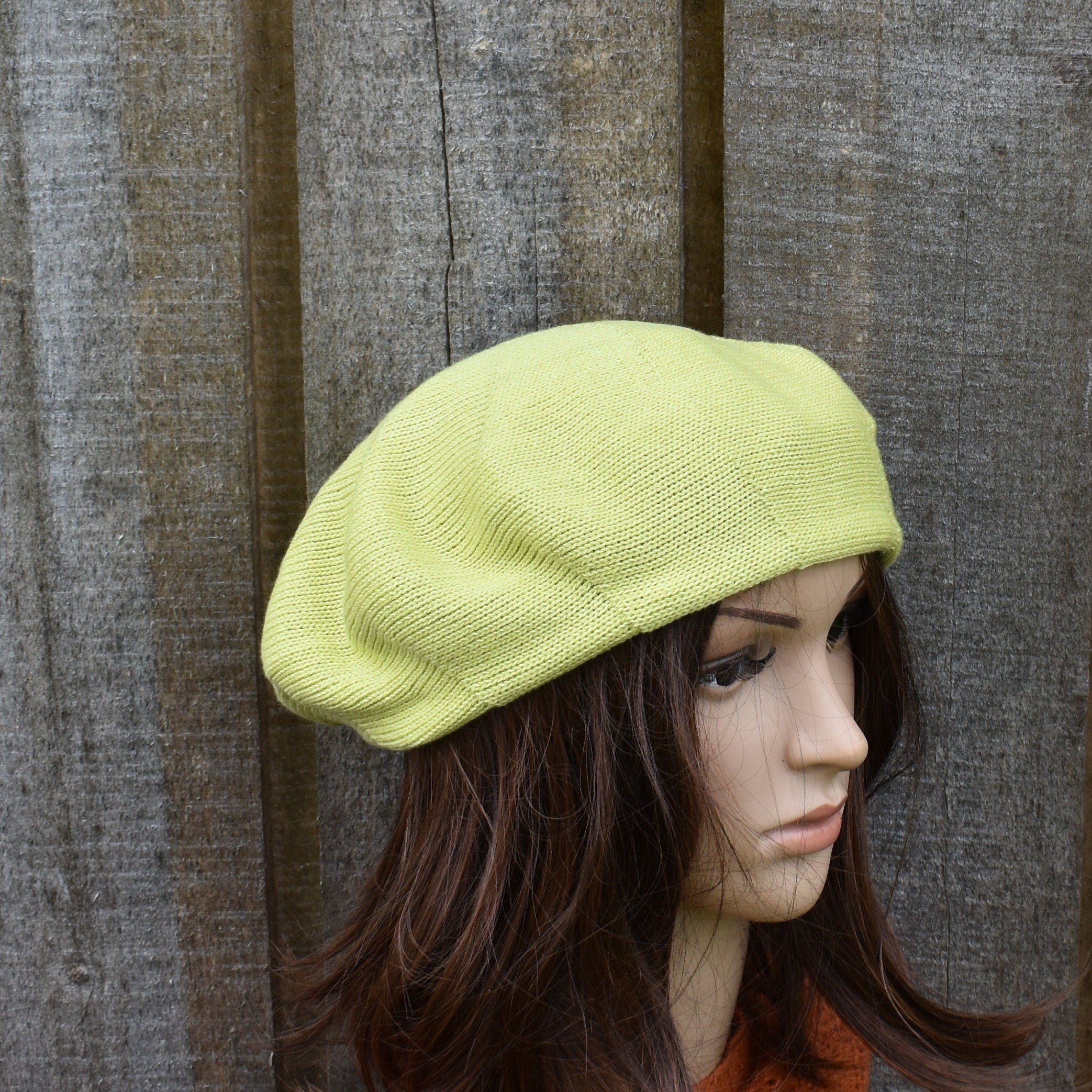 Person wearing a light green beret against a wooden background