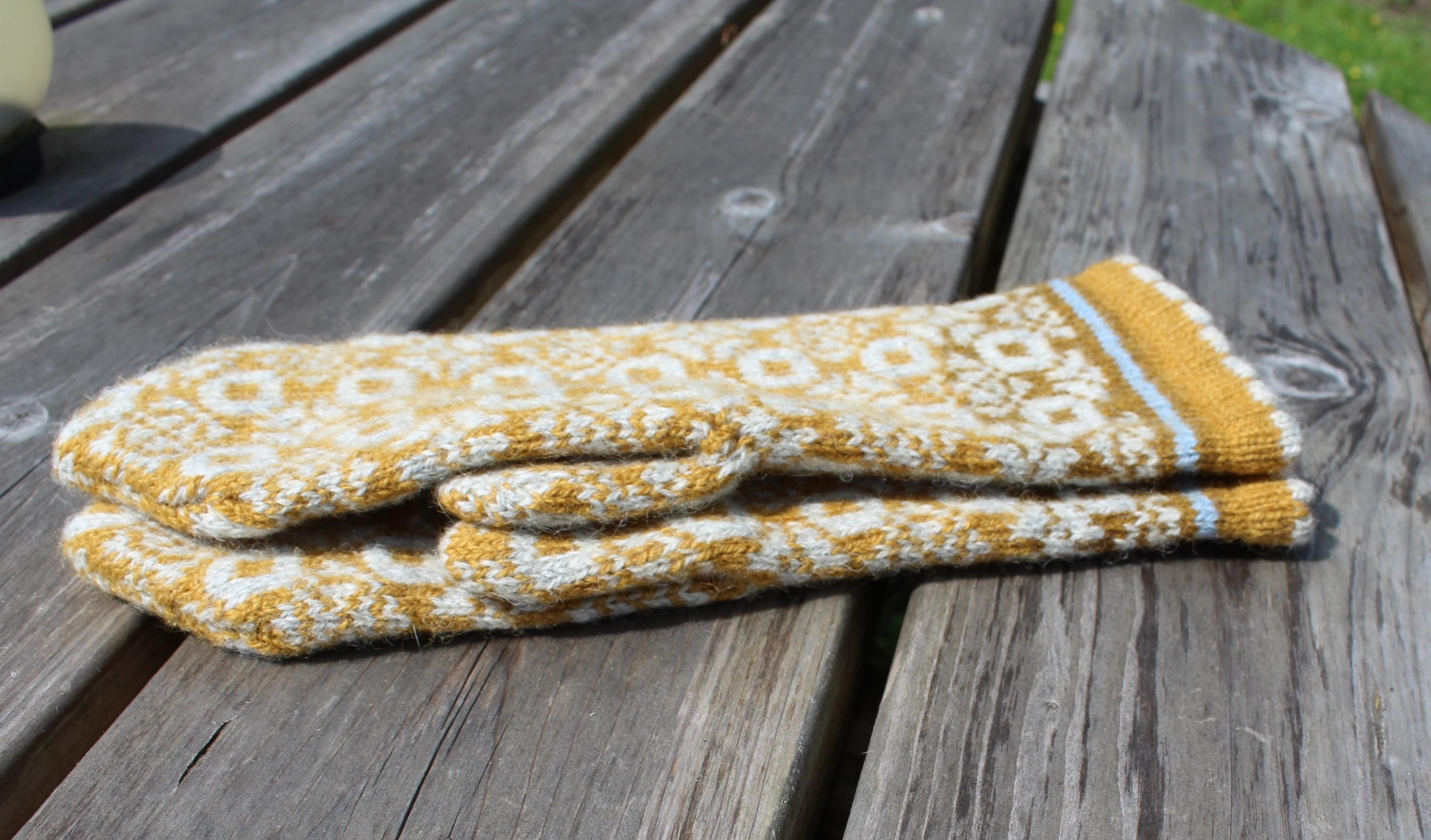 Pair of yellow and white patterned oven mitts on a wooden surface