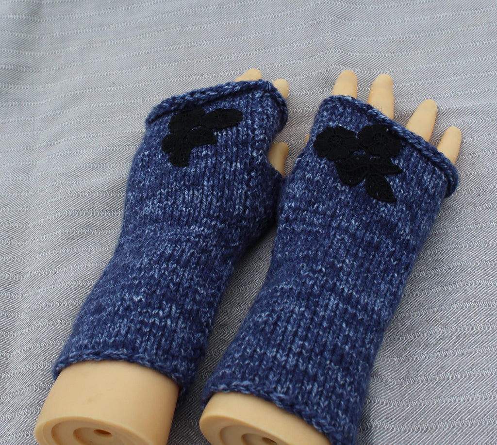 Blue knitted fingerless gloves with black flower decorations on a gray background
