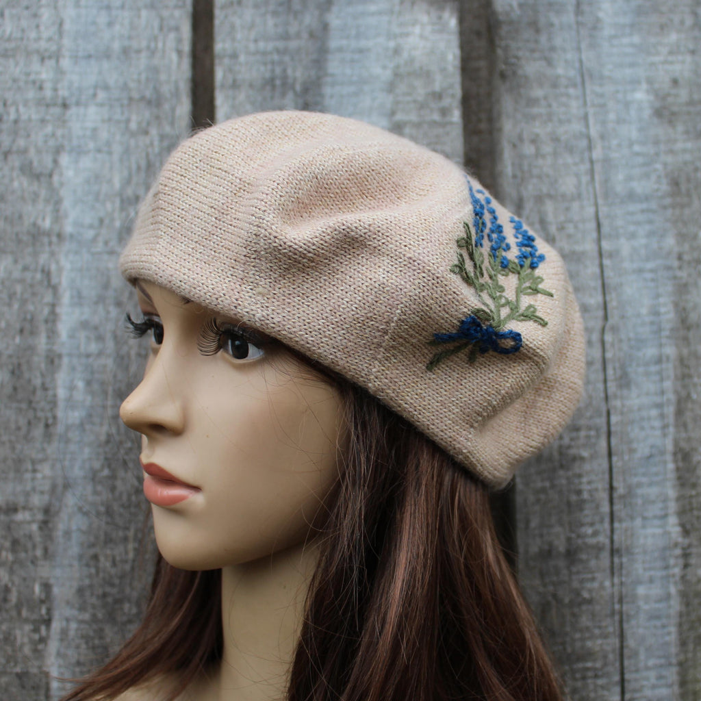 Beige knitted hat with floral embroidery on a mannequin head against a wooden background