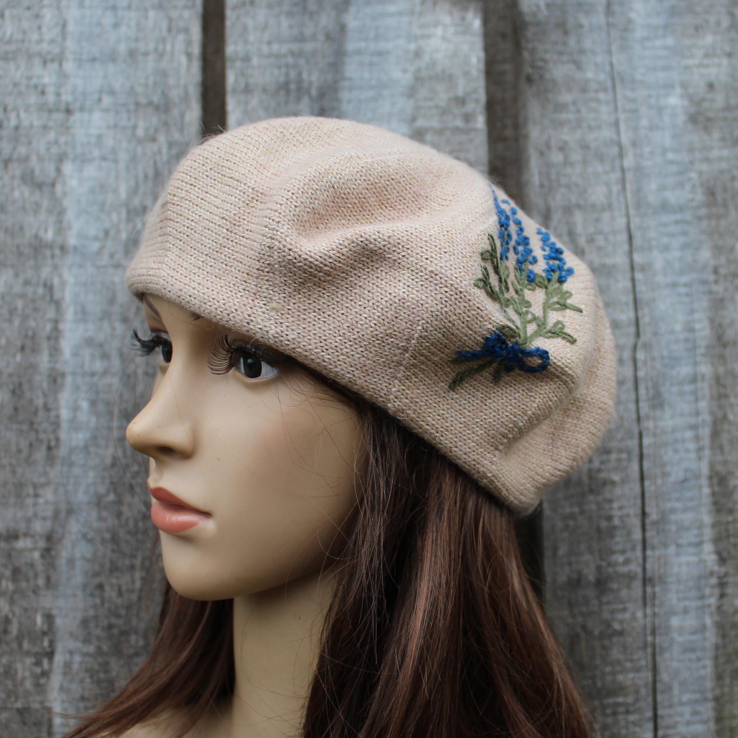 Beige knitted hat with floral embroidery on a mannequin head against a wooden background