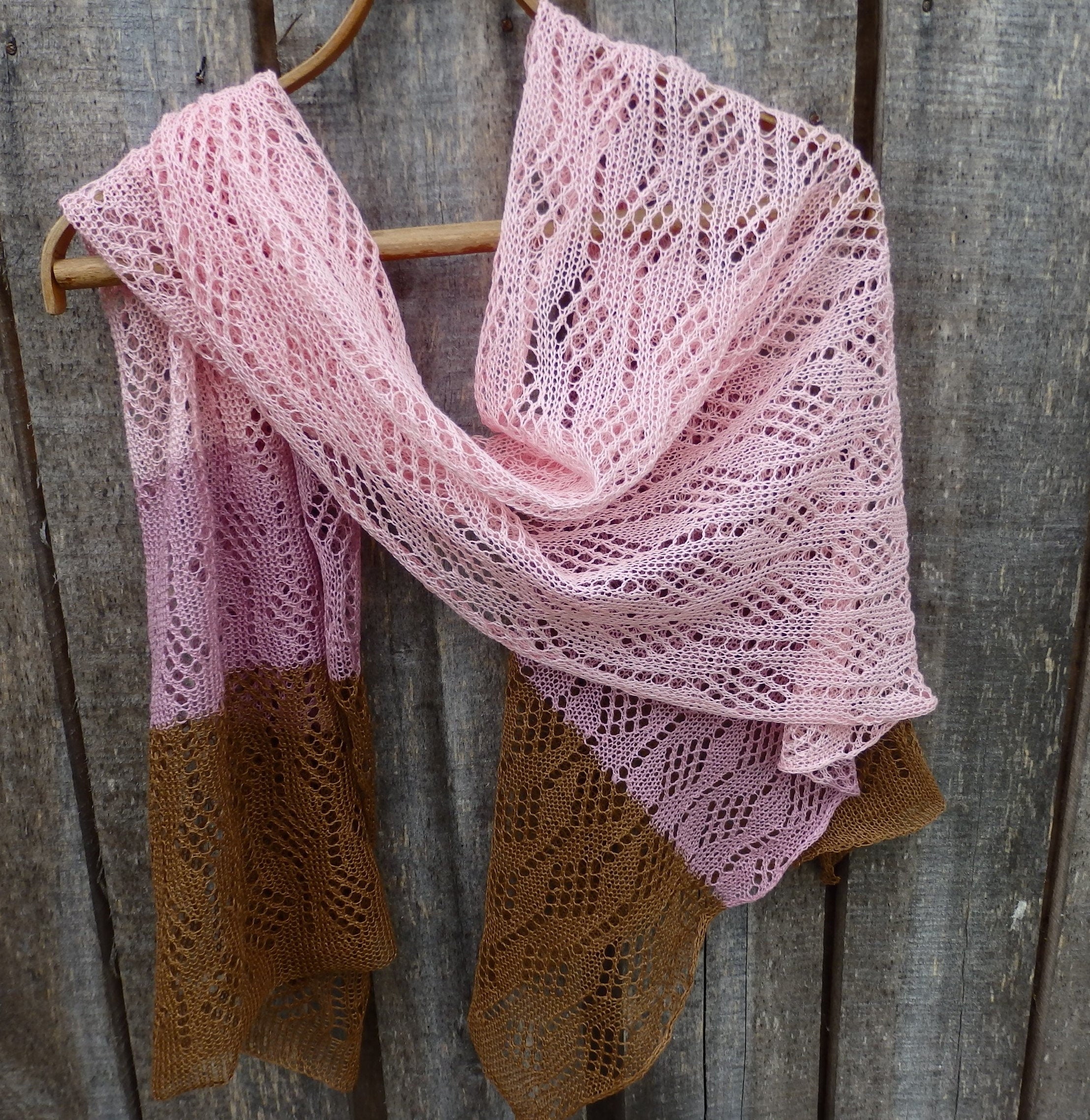 Pink and brown knitted shawl hanging on a wooden surface