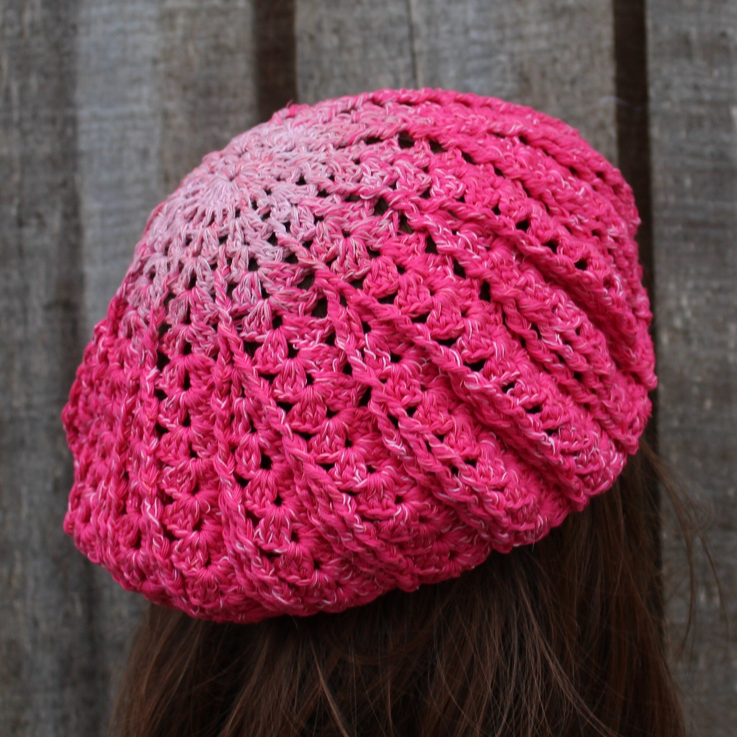 Pink crocheted cap worn by a person against a wooden fence background