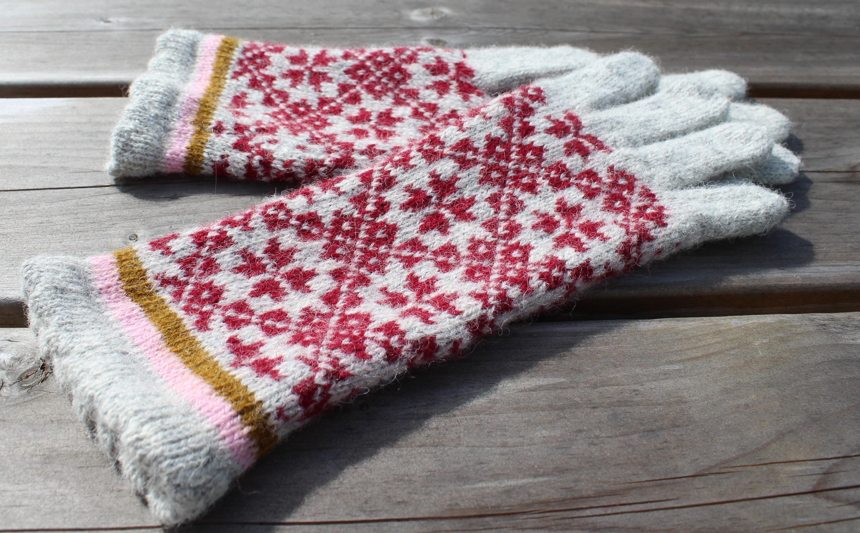 Pair of gloves with a red and white pattern on a wooden surface