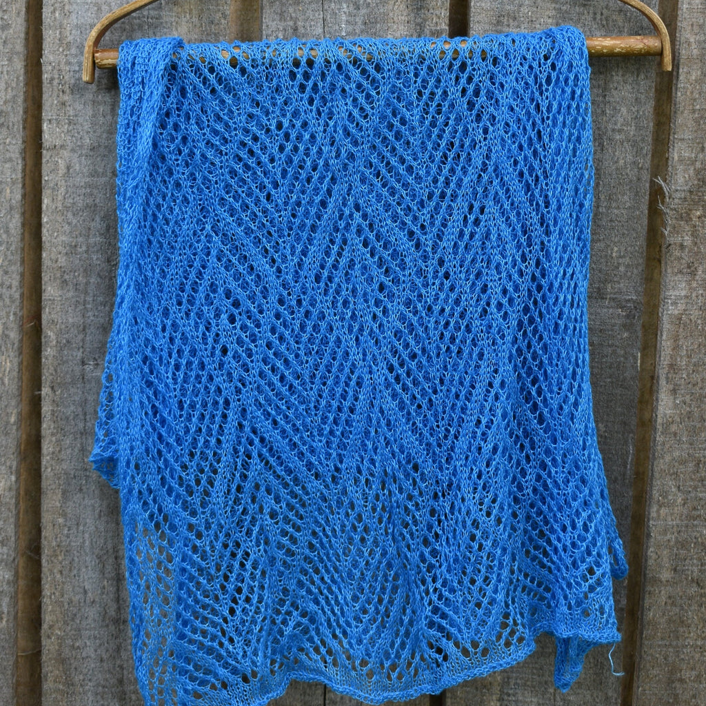 Blue knitted shawl on a wooden hanger against a wooden background
