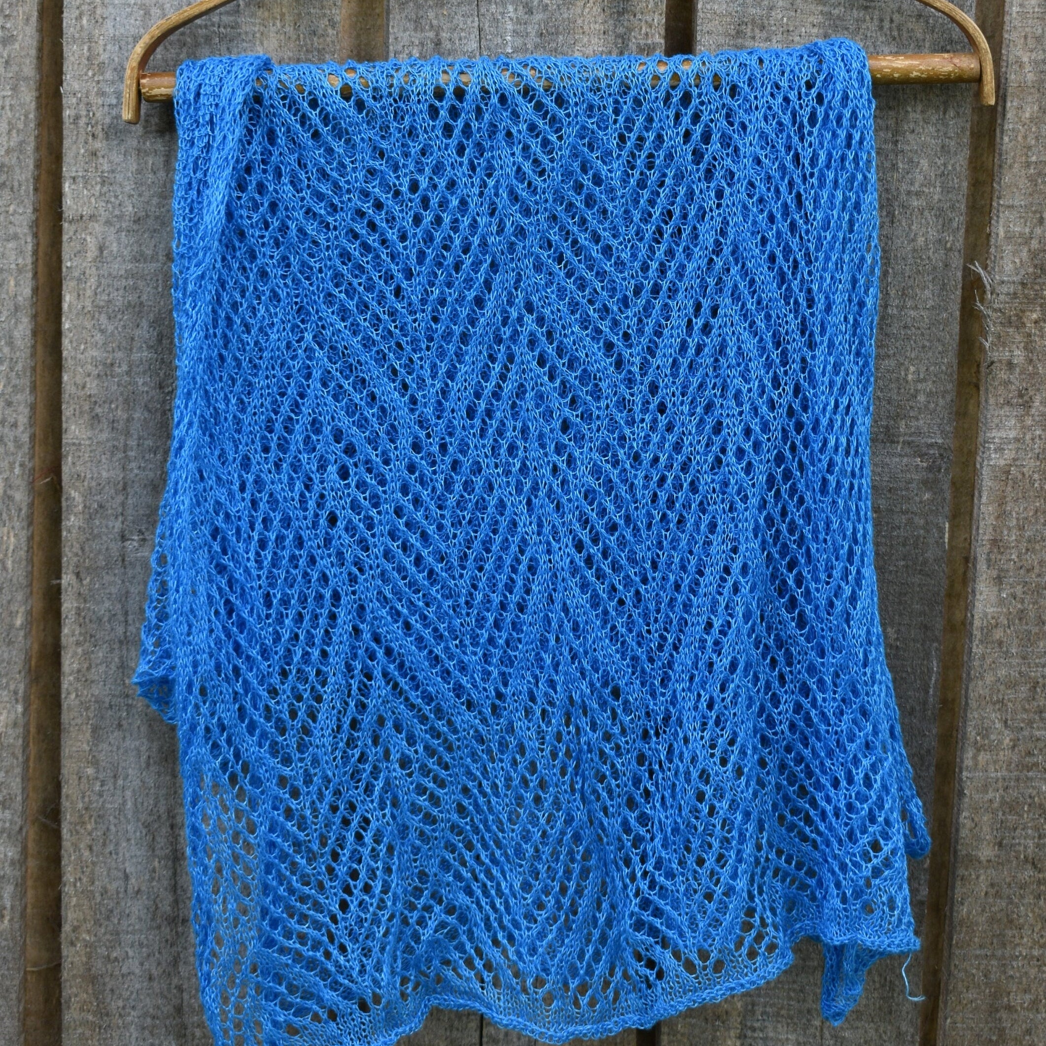 Blue knitted shawl on a wooden hanger against a wooden background