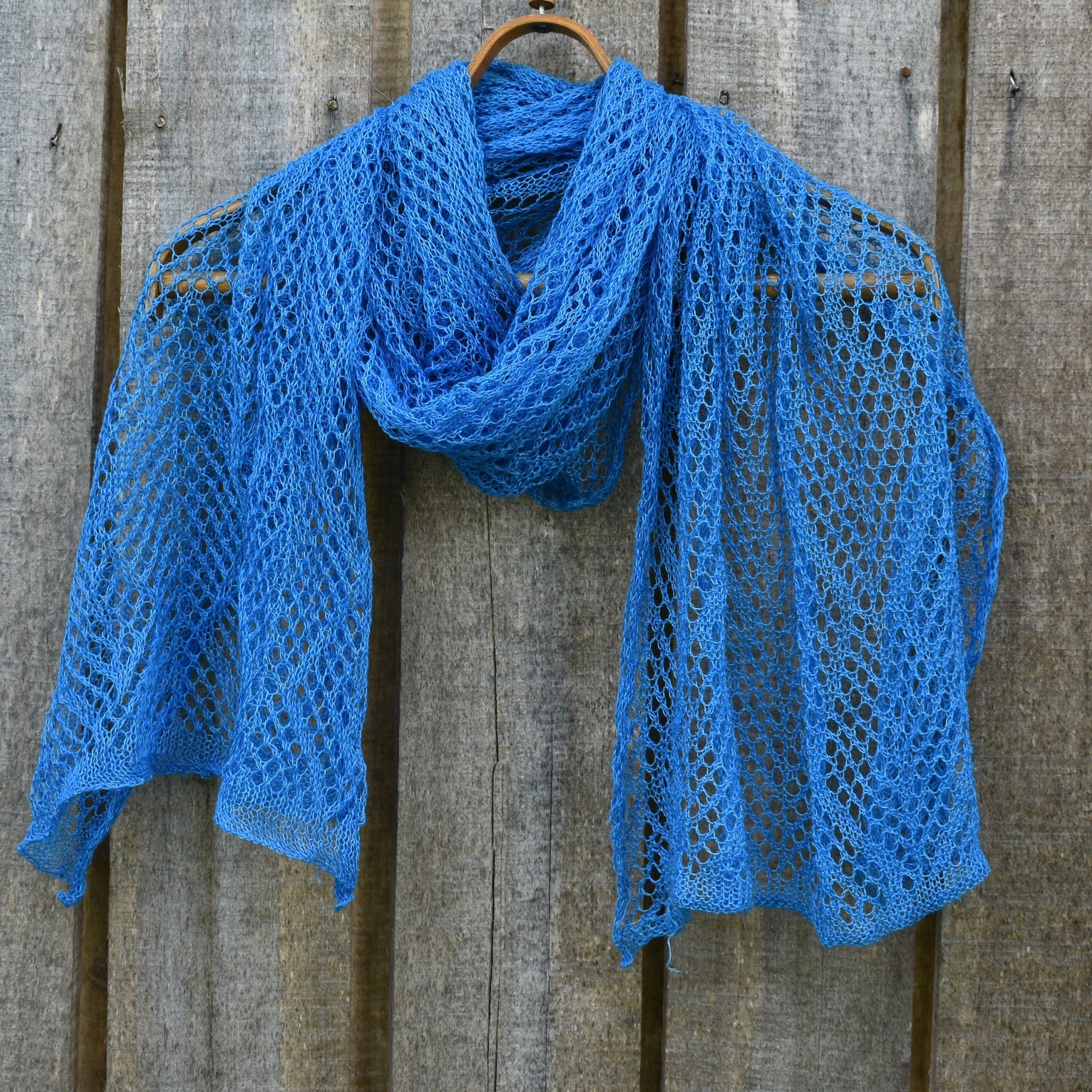 Blue knitted shawl on a wooden hanger against a wooden background